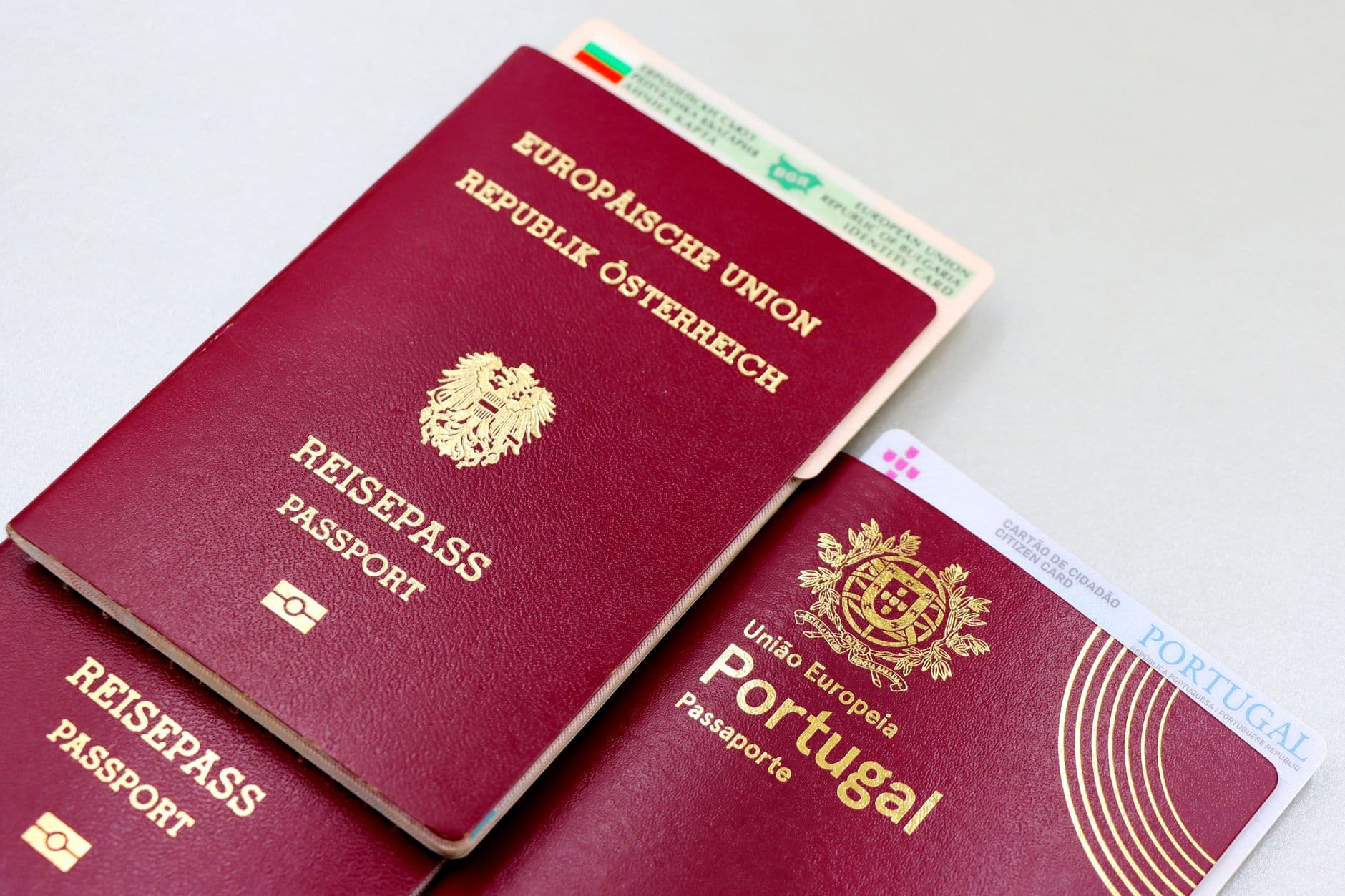 Mai multe pasapoarte europene rosii ale Austriei si Portugaliei, alaturi de carti de identitate, asezate pe o masa alba