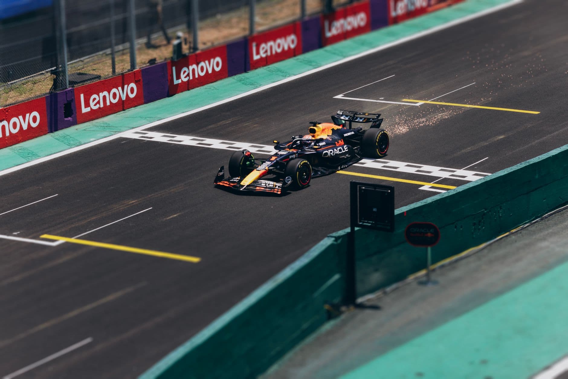 Monopost de Formula 1 Red Bull trecand linia de start pe un circuit de curse, cu scantei in spate si reclame Lenovo pe margine