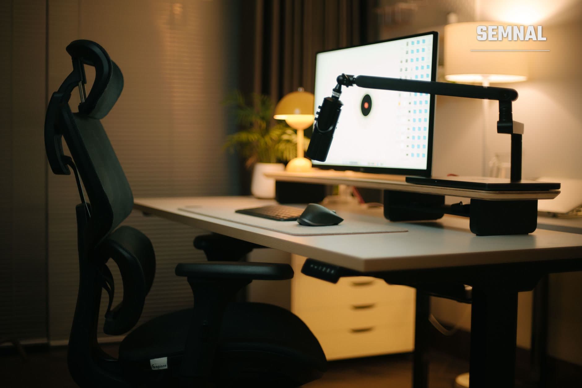 Birou ergonomic cu scaun negru, monitor pe braț articulat și periferice, aranjat pentru lucrul la calculator într-un mediu de birou modern cu iluminare caldă.
