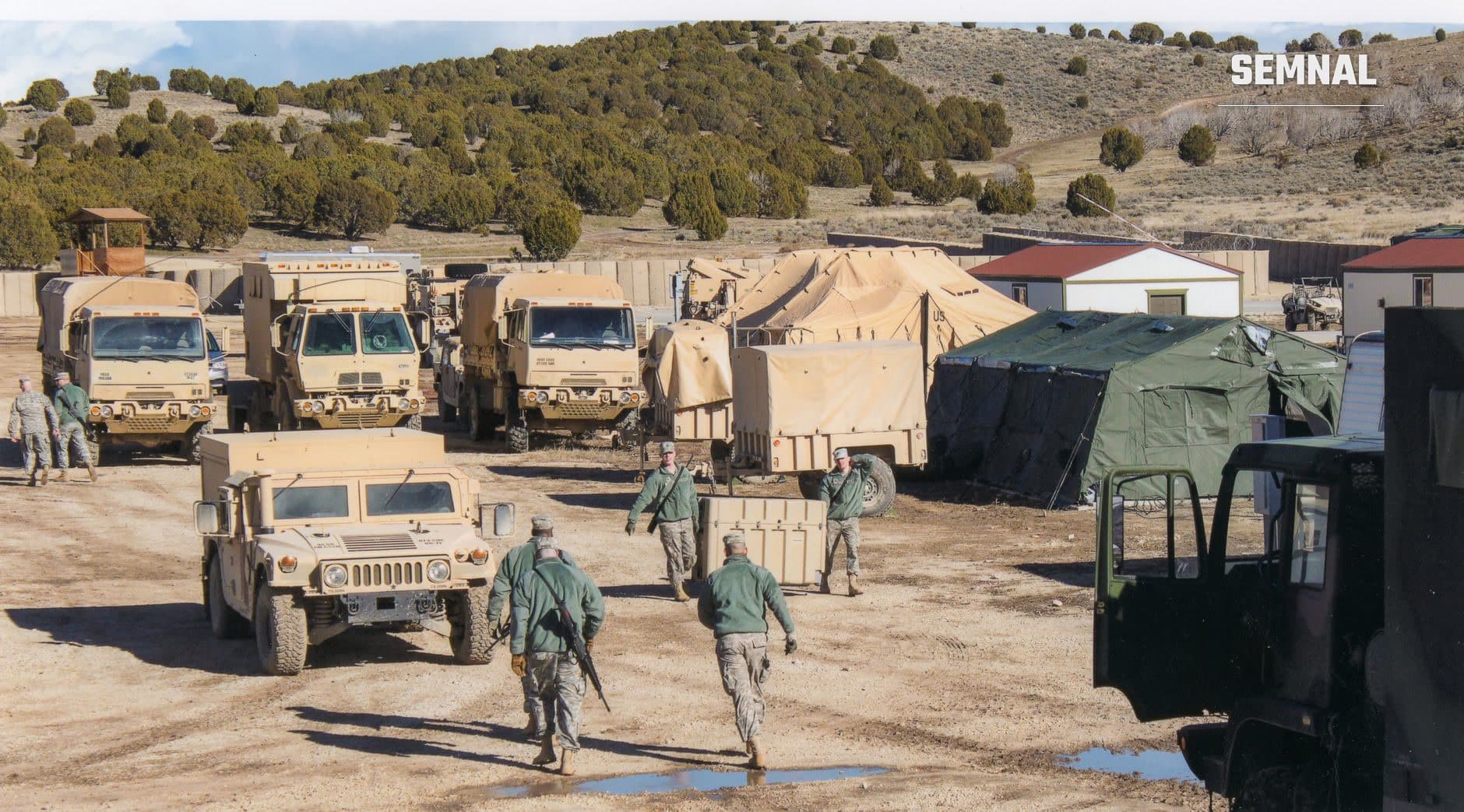 Bază militară NATO cu vehicule blindate, soldați și corturi de cazare pe teren steril din Estul Europei, ilustrând infrastructura și costurile operaționale ale prezentei militare americane.