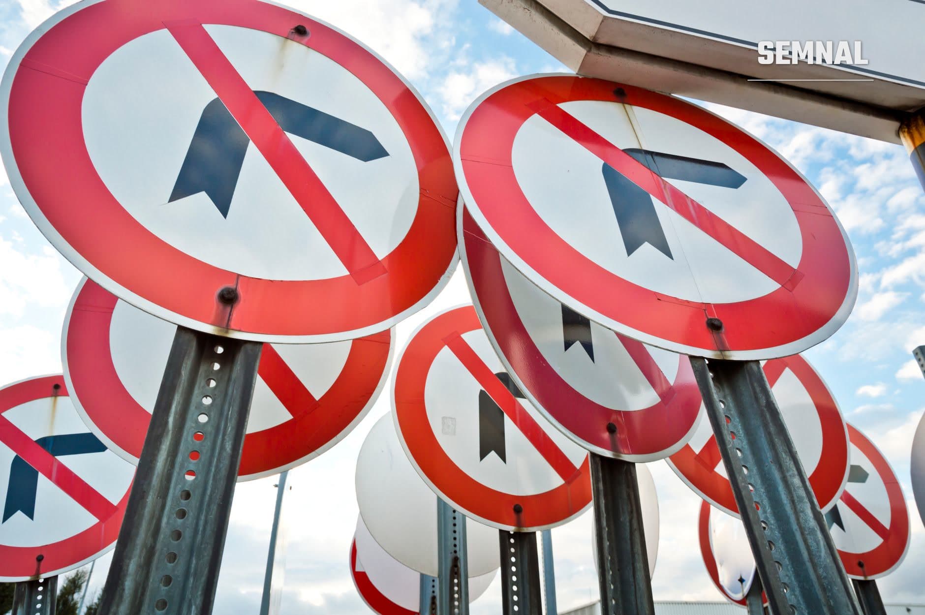 Semne de circulație rutieră roșii cu săgeți negre și diagonale, montate pe stâlpi metalici, indicând restricții și reglementări în trafic