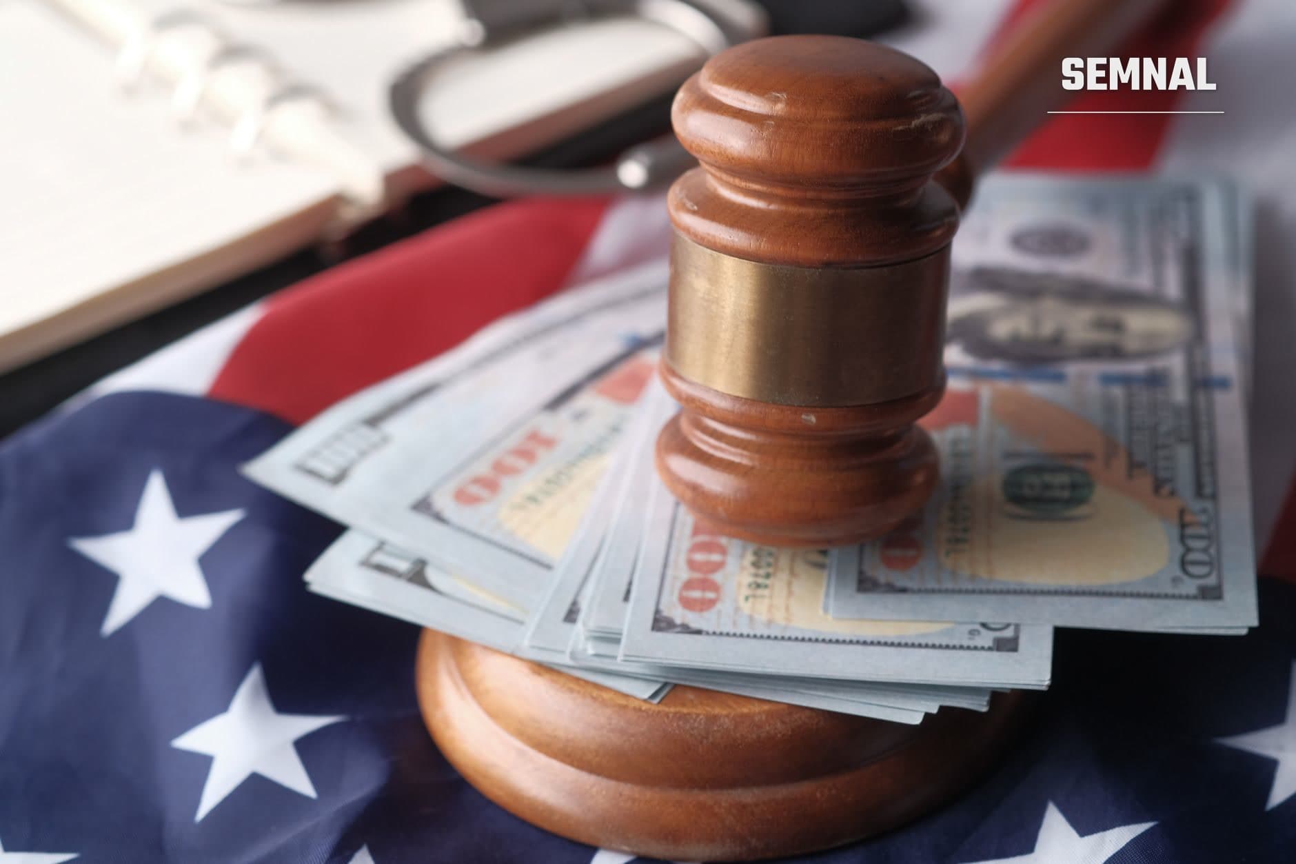 Ciocan de judecător din lemn pe bancnote de 100 de euro și drapelă americană, simbolizând justiția și sancțiunile financiare în procedurile legale de poprire