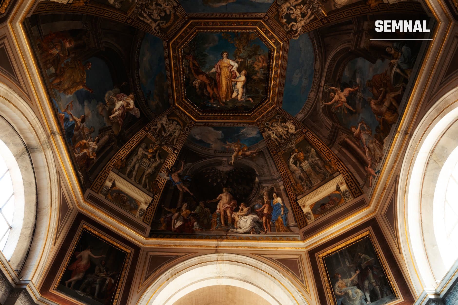 Plafon baroc ornamentat cu fresce și picturi mitologice în cadre aurii, cu decor geometric și figuri în stil Renaștere târzie, din interiorul unei clădiri istorice.