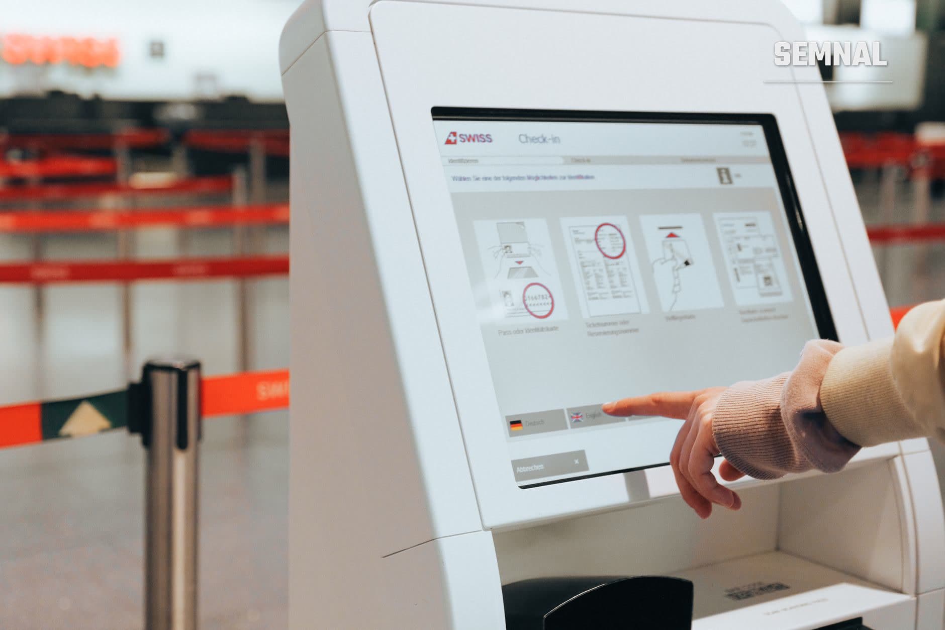 Pasager folosind terminalul de check-in SWISS cu ecran tactil pentru a-și alege locul la avion, cu cozi de așteptare vizibile în fundal