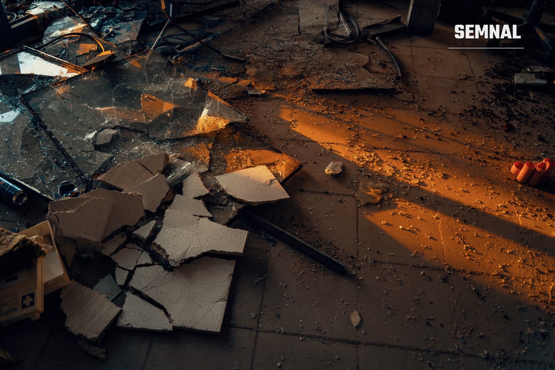 Rămășițe și moloz negru și portocaliu după o explozie, cuprinzând fragmente metalice arse și praf pe sol murdar, ilustrând devastarea unui atac aerian.
