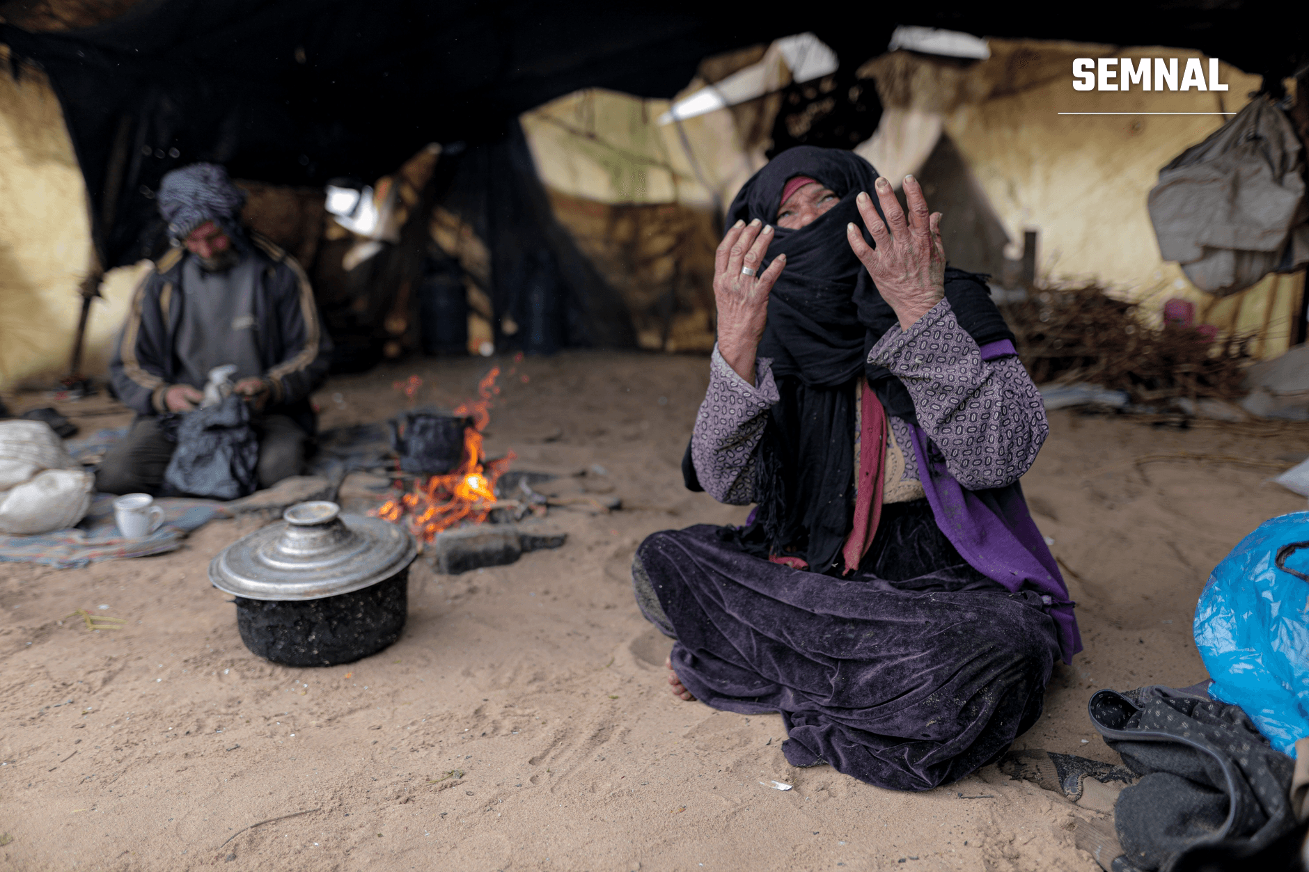 Femeie în niqab negru cu mâinile ridicate, în corturi și tabărcum de refugiați din Gaza, ilustrând situația umanitară a civili palestinieni strămutați.