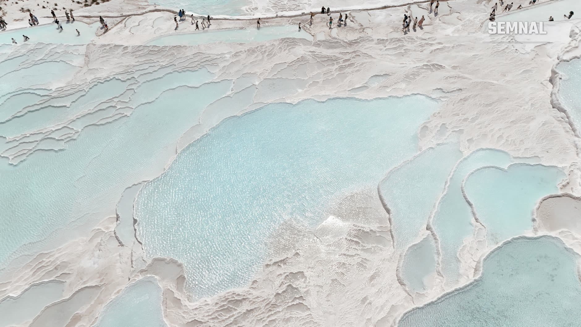 Cascade de apă termală cu depozite minerale albe și bazine de apă turcoaz, fotografie aeriană a unei surse naturale de apă bogată în minerale.
