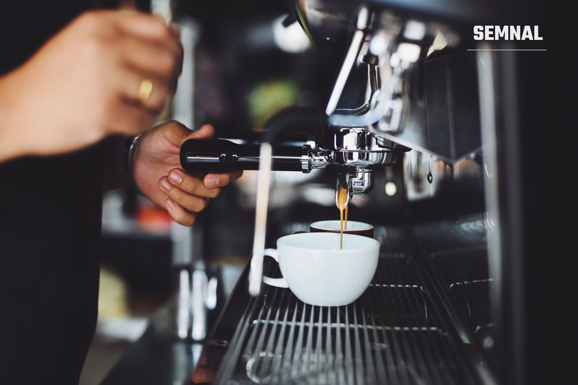 Barista pregătind o cană de espresso pe mașina de cafea profesională, cu lichid auriu curgând în ceașcă albă, într-o cafenea de specialitate