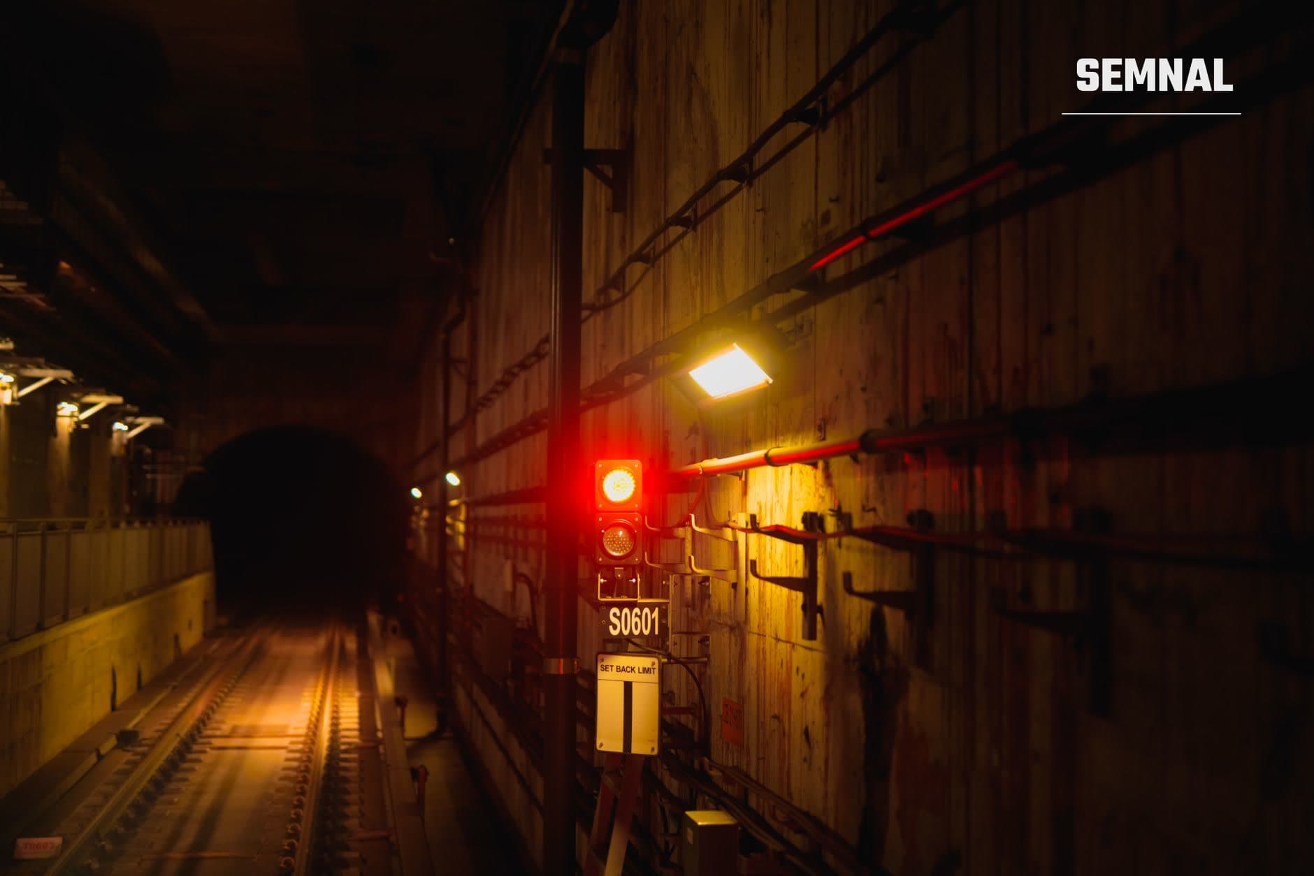 Tunel subteran cu cale ferată și semnalizare roșie și galbenă iluminată noaptea, pereți de beton și marcaje industriale vizibile în infrastruktura subterană. (Foto: YIYANG LIU / Pexels)