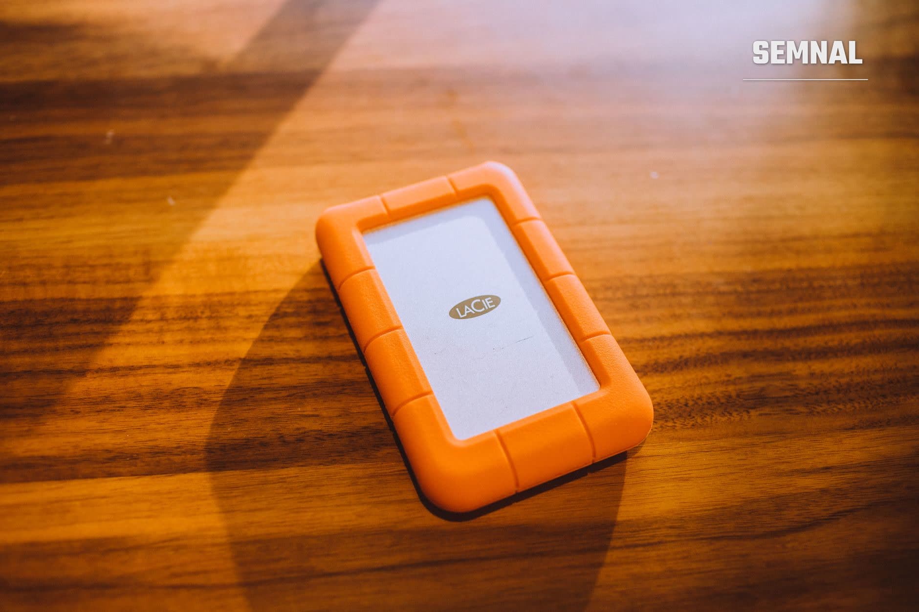 Unitate externă de stocare LaCie cu carcasă portocalie pe masă din lemn, echipament pentru backup și protecția datelor (Foto: Luis Quintero / Pexels)