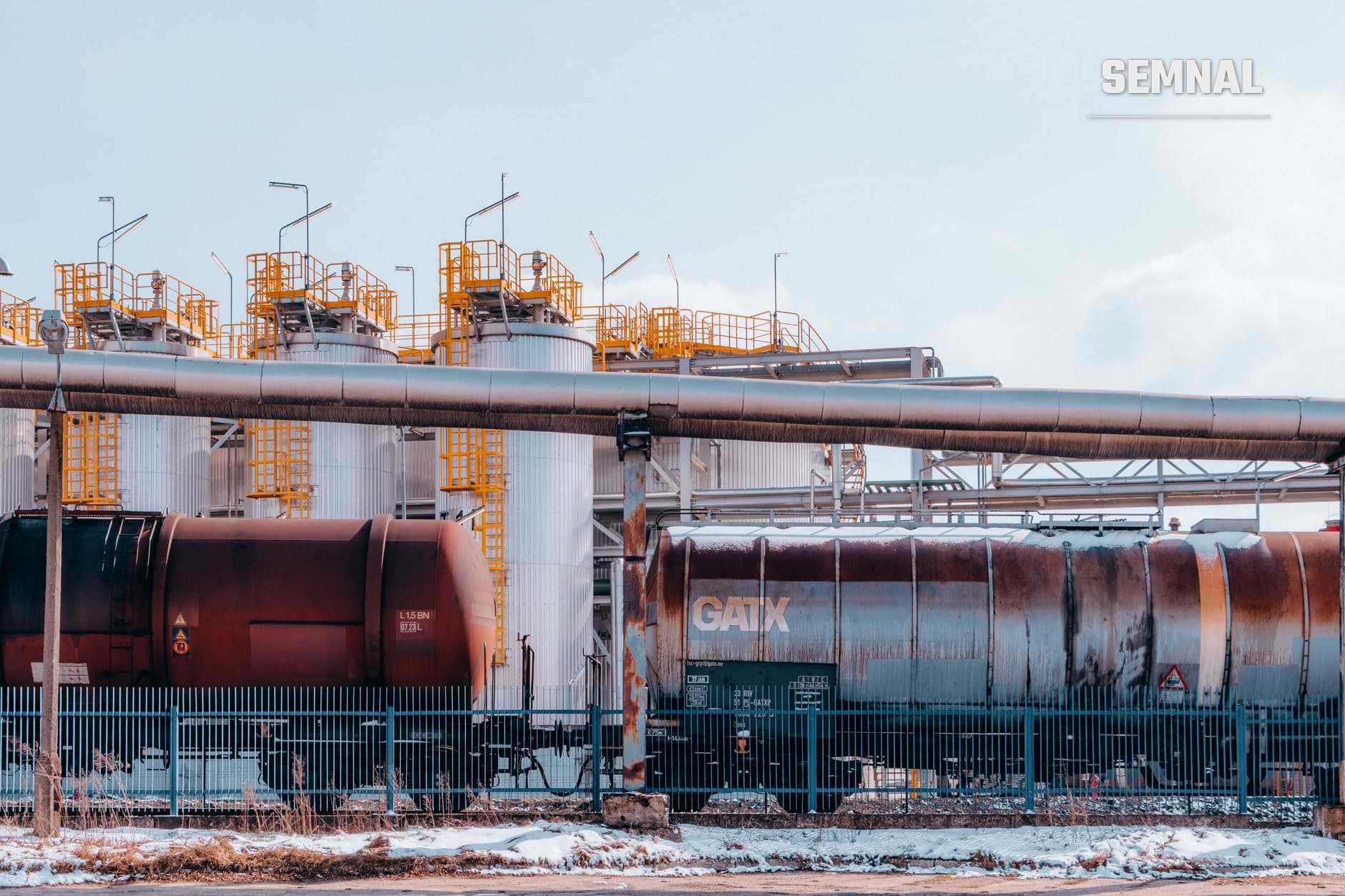 Instalație industrială de stocare petrolier cu mari cisterne cilindrice metalice marcate CAIX, platforme de lucru portocalii și conducte de transport, într-o zi iernă cu ușoară înzăpezire pe teren. (Foto: Jakub Pabis / Pexels)