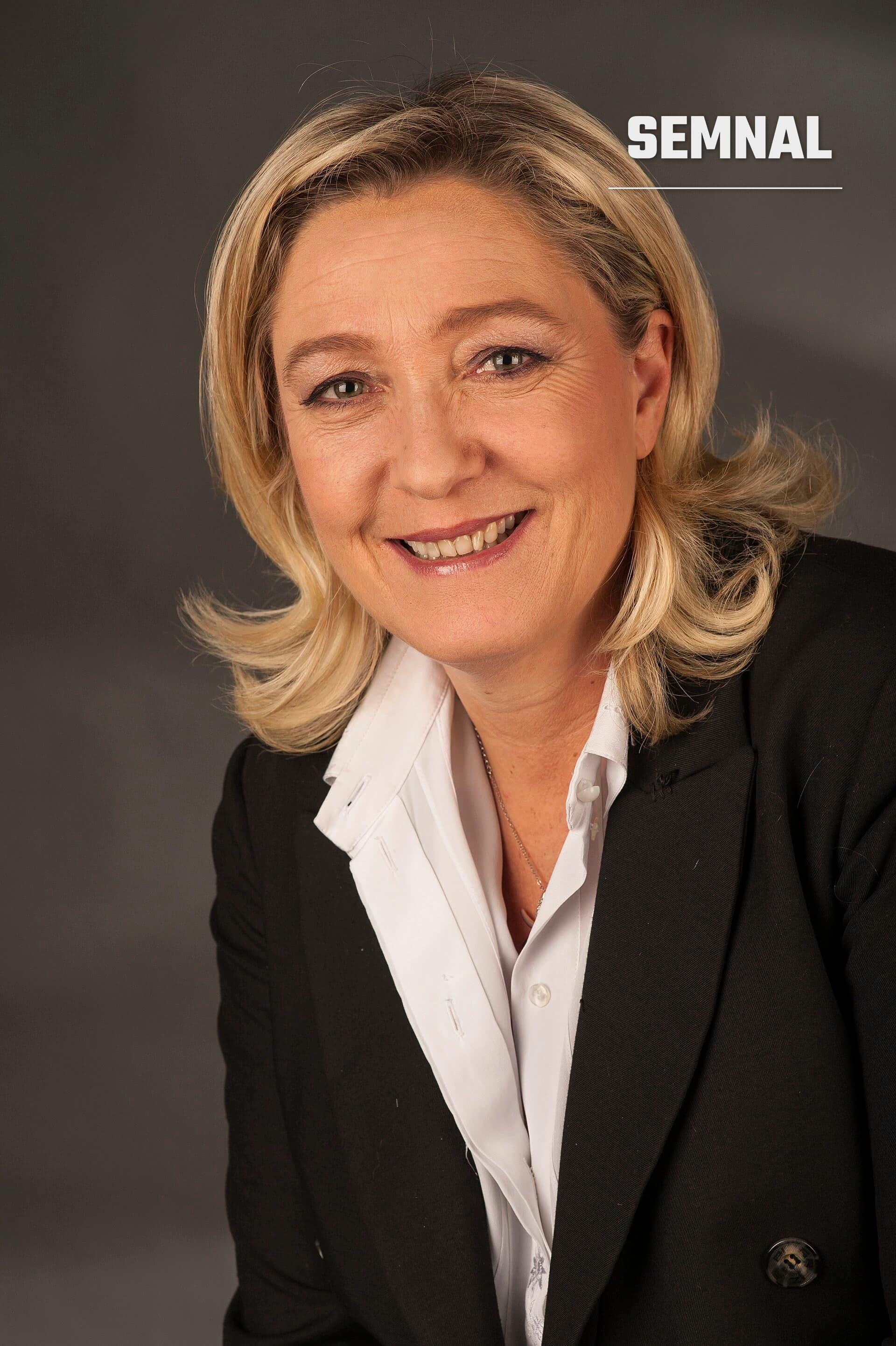 Marine Le Pen, portret oficial în costum negru și cămașă albă, zâmbând la cameră pe fond gri neutru. (Foto: Foto-AG Gymnasium Melle)