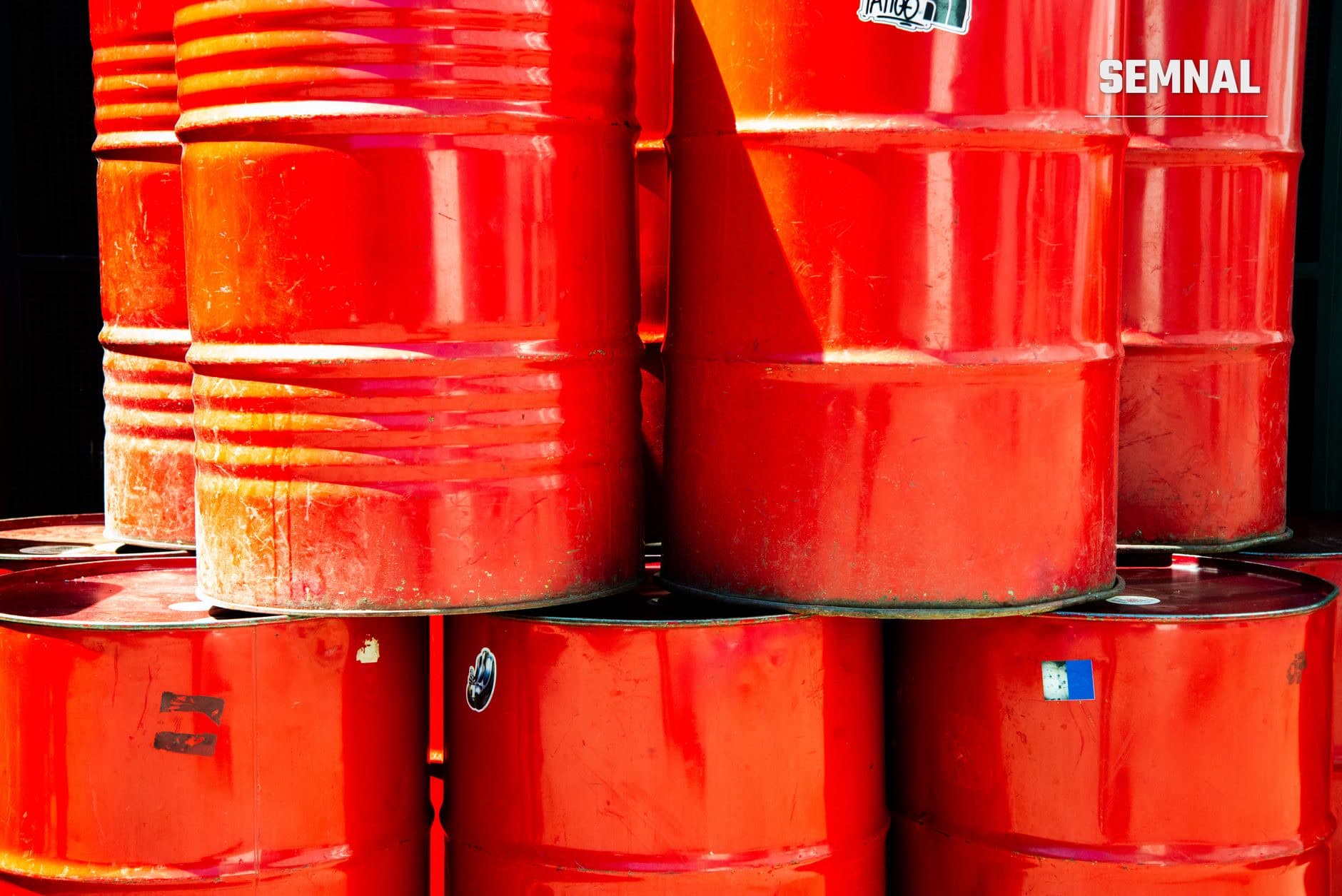 Stivă de butoaie metalice roșii pentru transport și depozitare petrol, stivuite pe platformă industrială, marcate cu etichete de identificare. (Foto: Александр Лич / Pexels)
