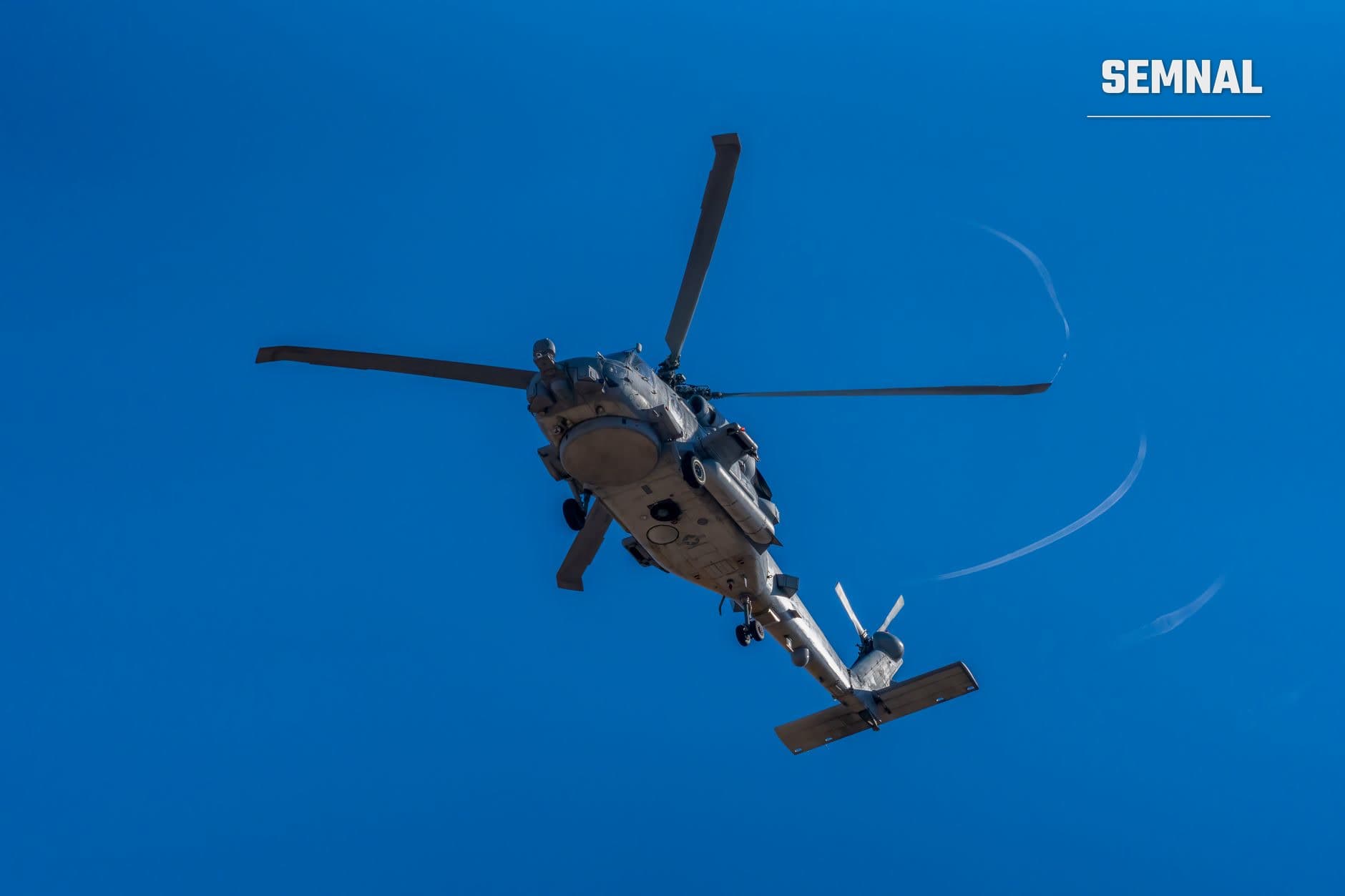 Elicopter militar gri-alb în zbor pe cer albastru, fotografiat din jos, cu patru pale rotative și fuselaj detaliat vizibil. (Foto: Rafael Minguet Delgado / Pexels)