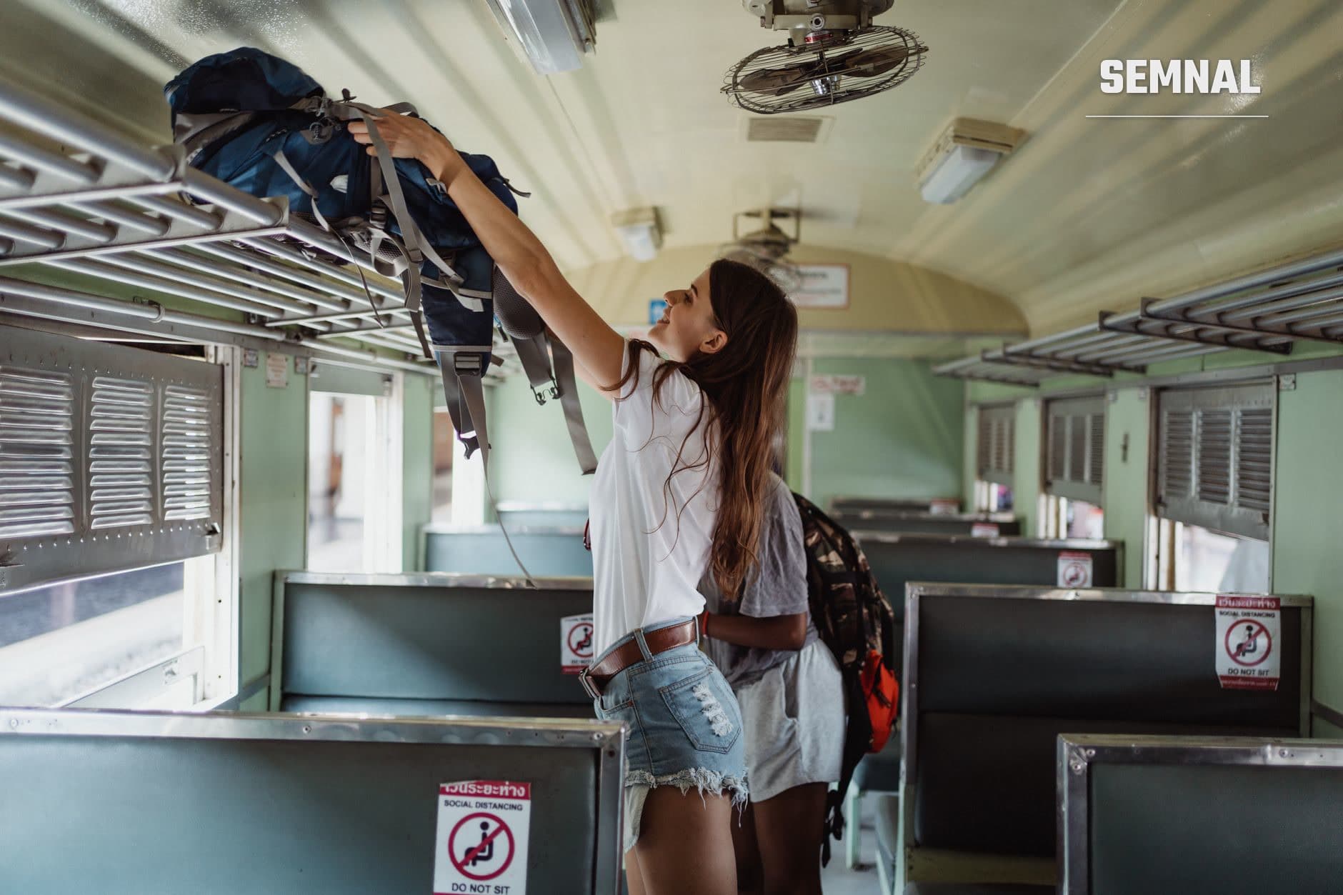 O femeie cu rucsac de drumeții albastru-negru sus deasupra unui scaun într-o cabină de autobuz cu pereți verzui și semne de distanțare socială (Foto: Ketut Subiyanto / Pexels)