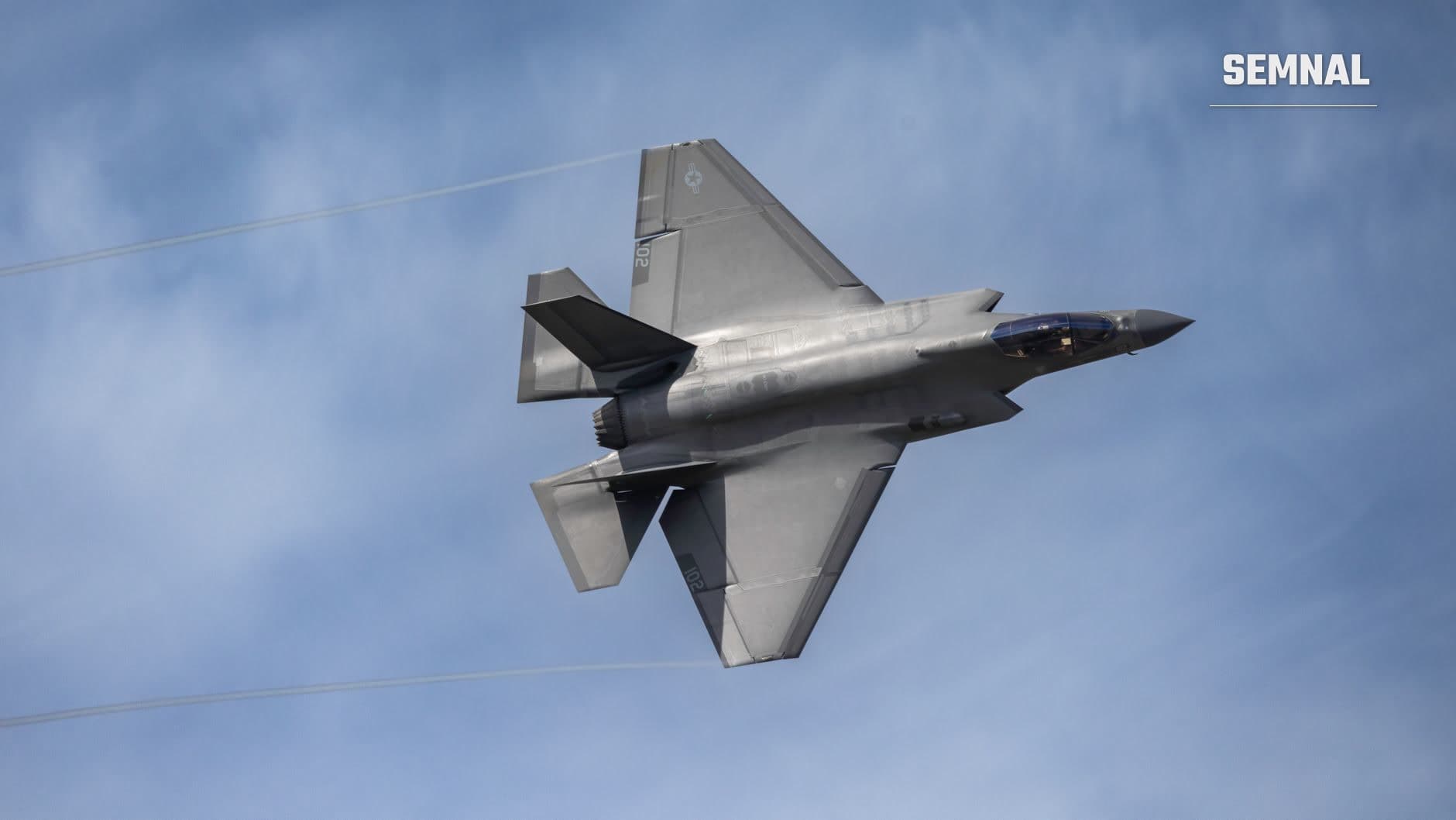 Avion de vânătoare F-35 Lightning II în zbor, fotografiat de jos pe cer albastru, arătând designul argintiu și aripile delta caracteristice acestui avion stealth american de generația a cincea. (Foto: Guy  Seela / Pexels)