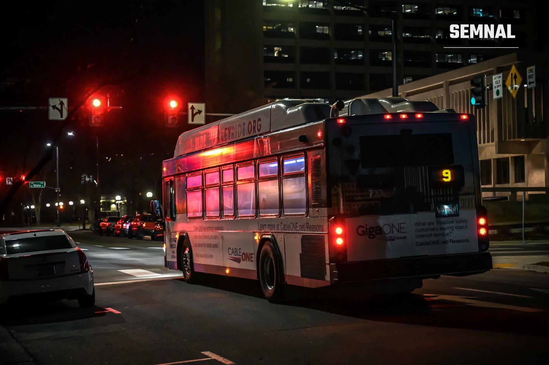 Doi autobuzi iluminați cu lumini roșii de oprire la o intersecție de noapte într-un mediu urban american, cu semafoare și clădiri în fundal. (Foto: Brett Sayles / Pexels)