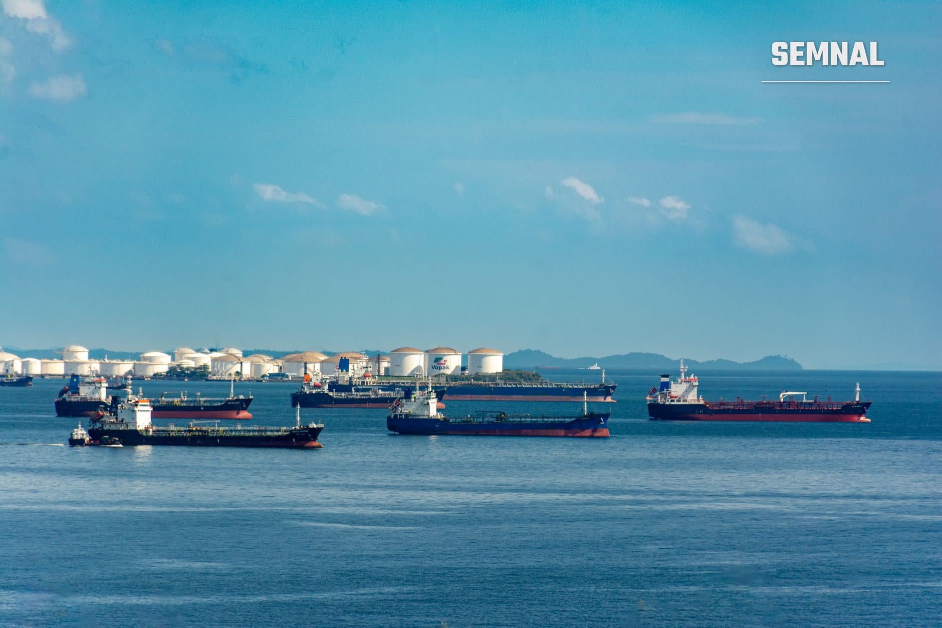 Patru tancuri petroliere de înaltă tonaj ancorate în apele unui port industrial, cu rezervoare cilindrice mari și echipamente portuare în fundal pe o zi cu cer senin și apă liniștită. (Foto: Zifeng Xiong / Pexels)