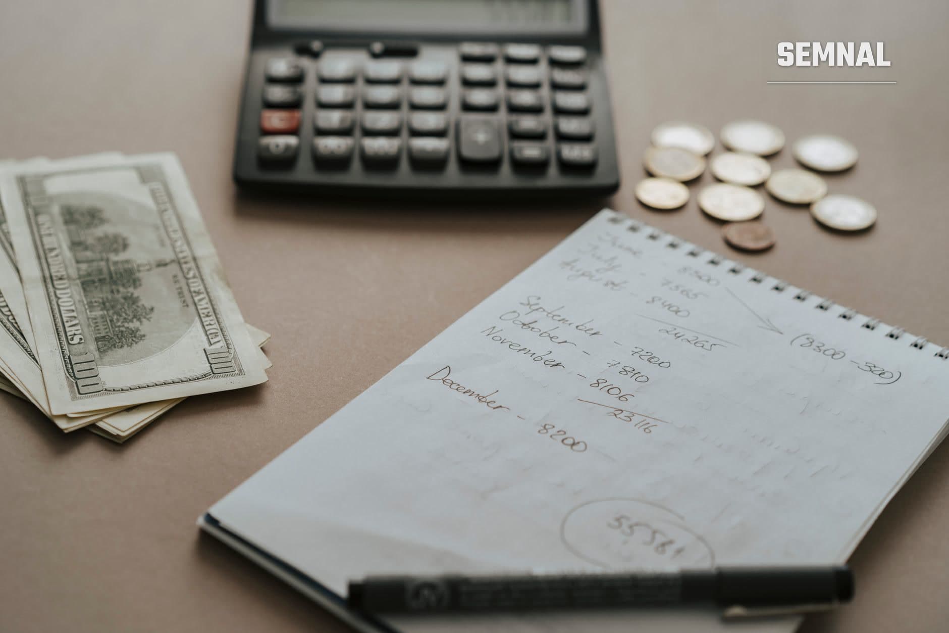 Birou cu caiet spiral conținând notații financiare, bancnote, calculator și monede, ilustrând planificarea unui buget lunar cu venituri variabile (Foto: olia danilevich / Pexels)