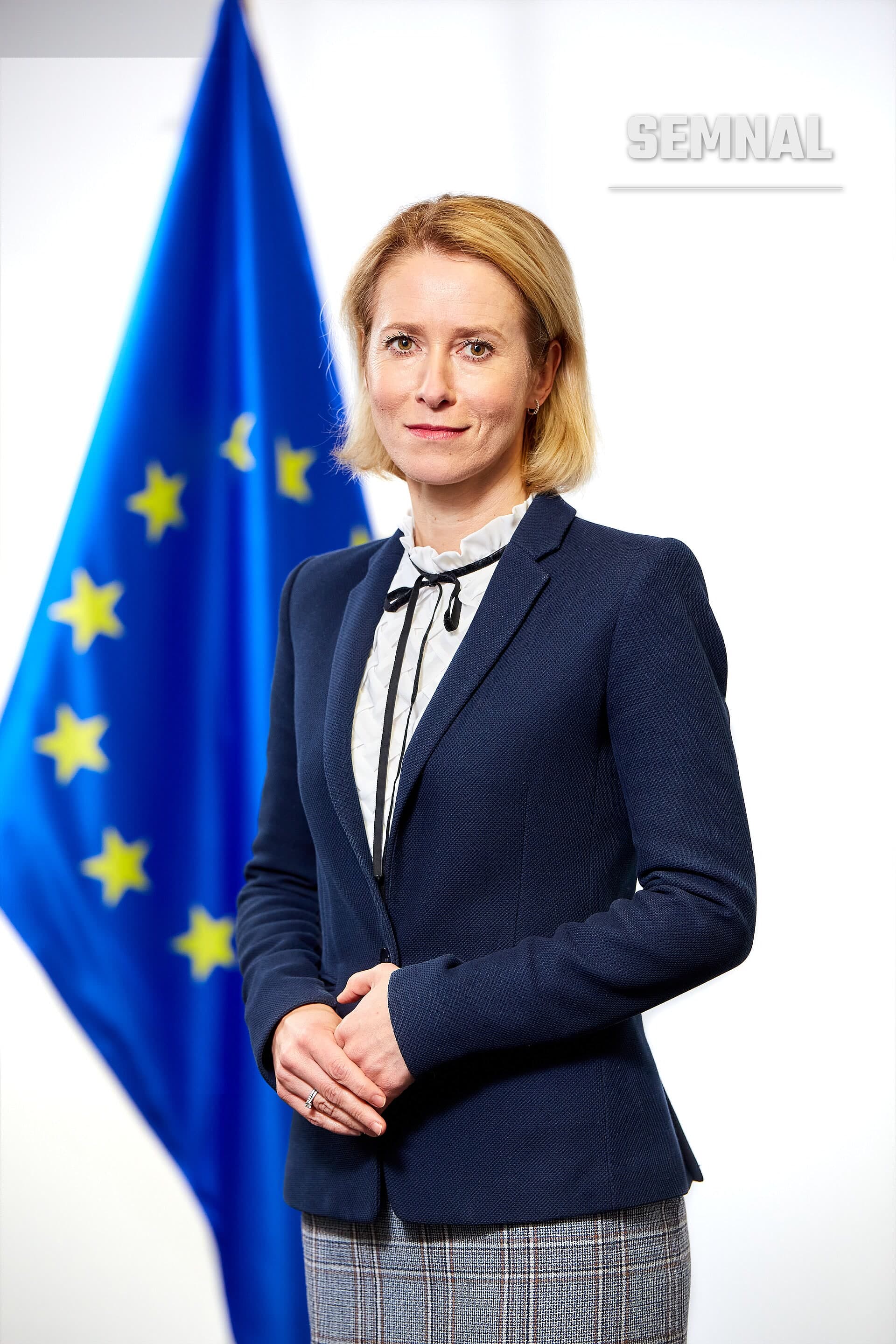 Kaja Kallas, șefa diplomației europene, într-un portret oficial purtând costum bleumarin și cămașă albă cu panglică, în fața steagului Uniunii Europene. (Foto: Aurore Martignoni / European Union)