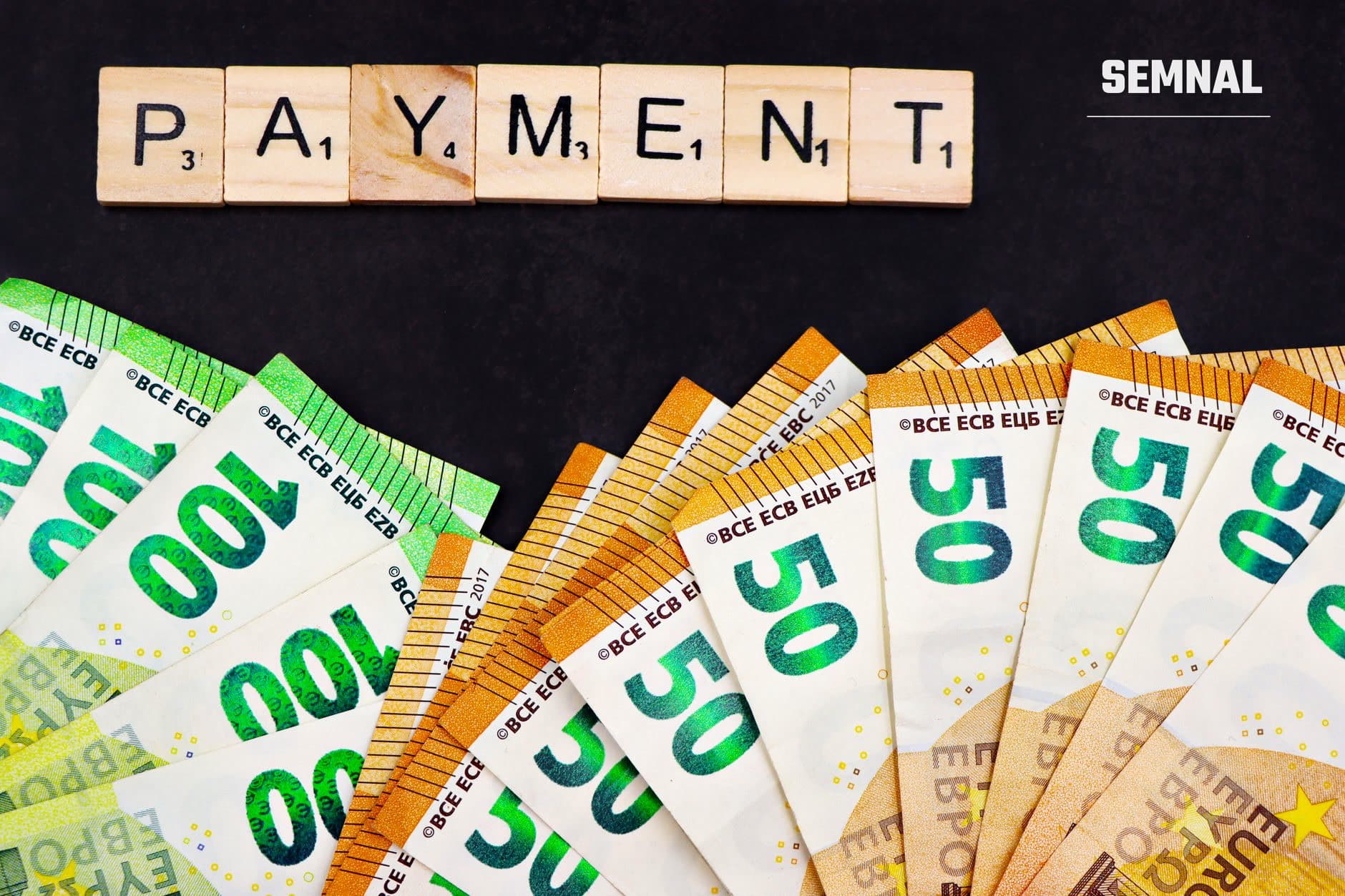 Cuvântul PAYMENT format din piese de joc Scrabble deasupra unor bancnote euro de diferite valori (50, 200 euro) de la Banca Centrală Europeană pe fundal negru. (Foto: Marta Branco / Pexels)