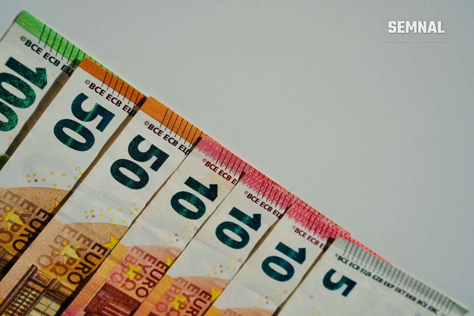 Bancnote euro de 50, 20 și 10 euro aranjate în evantai, cu marcajele de securitate și culori caracteristice fiecărei valori, pe fundal gri. (Foto: Ivan Vi / Pexels)
