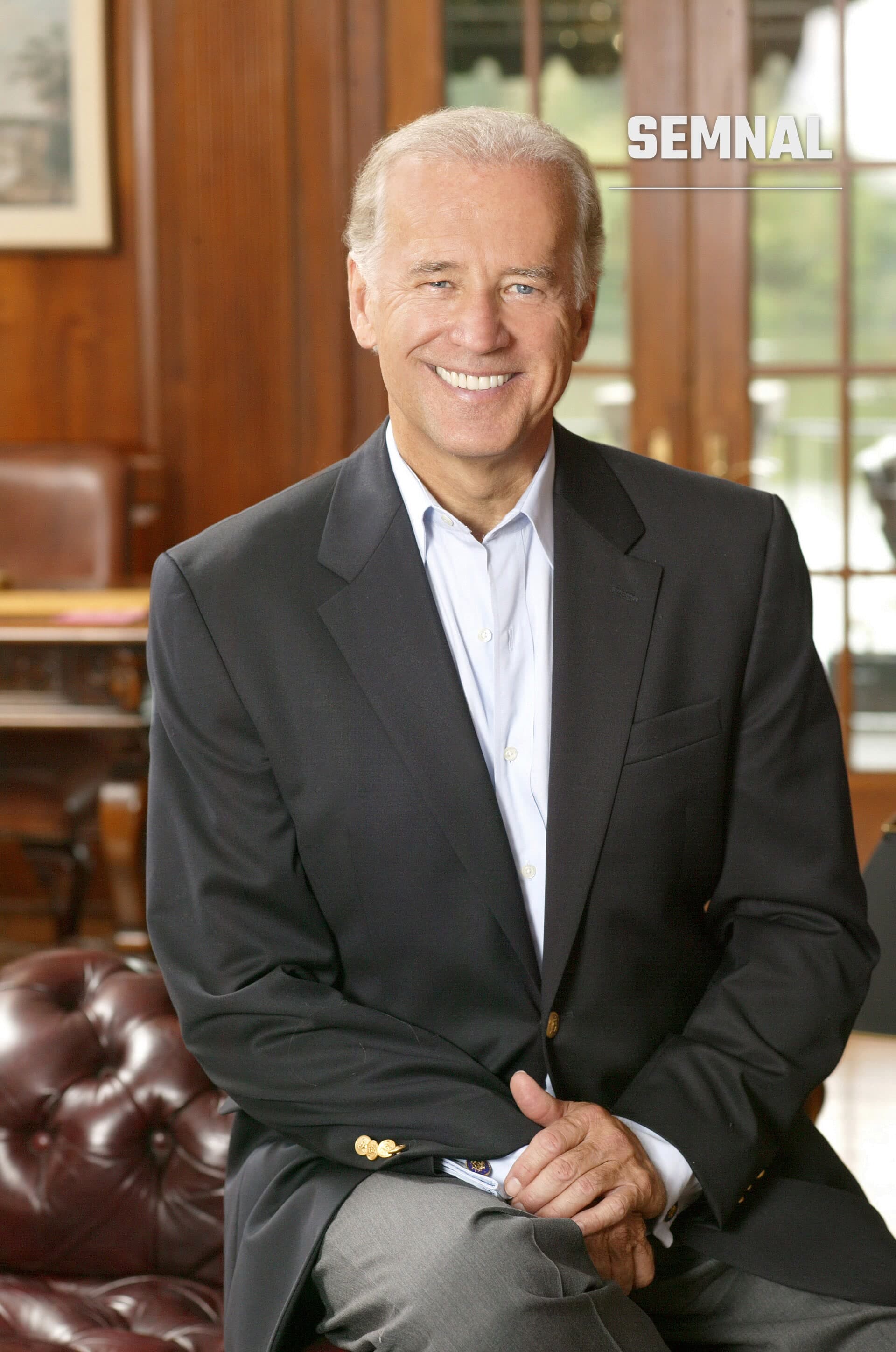 Joe Biden, bărbat în costum negru și cămașă albastră, zâmbind în portretul formal realizat într-un interior elegant cu mobilier din piele și ferestre cu perdele de lemn. (Foto: United States Senate.)
