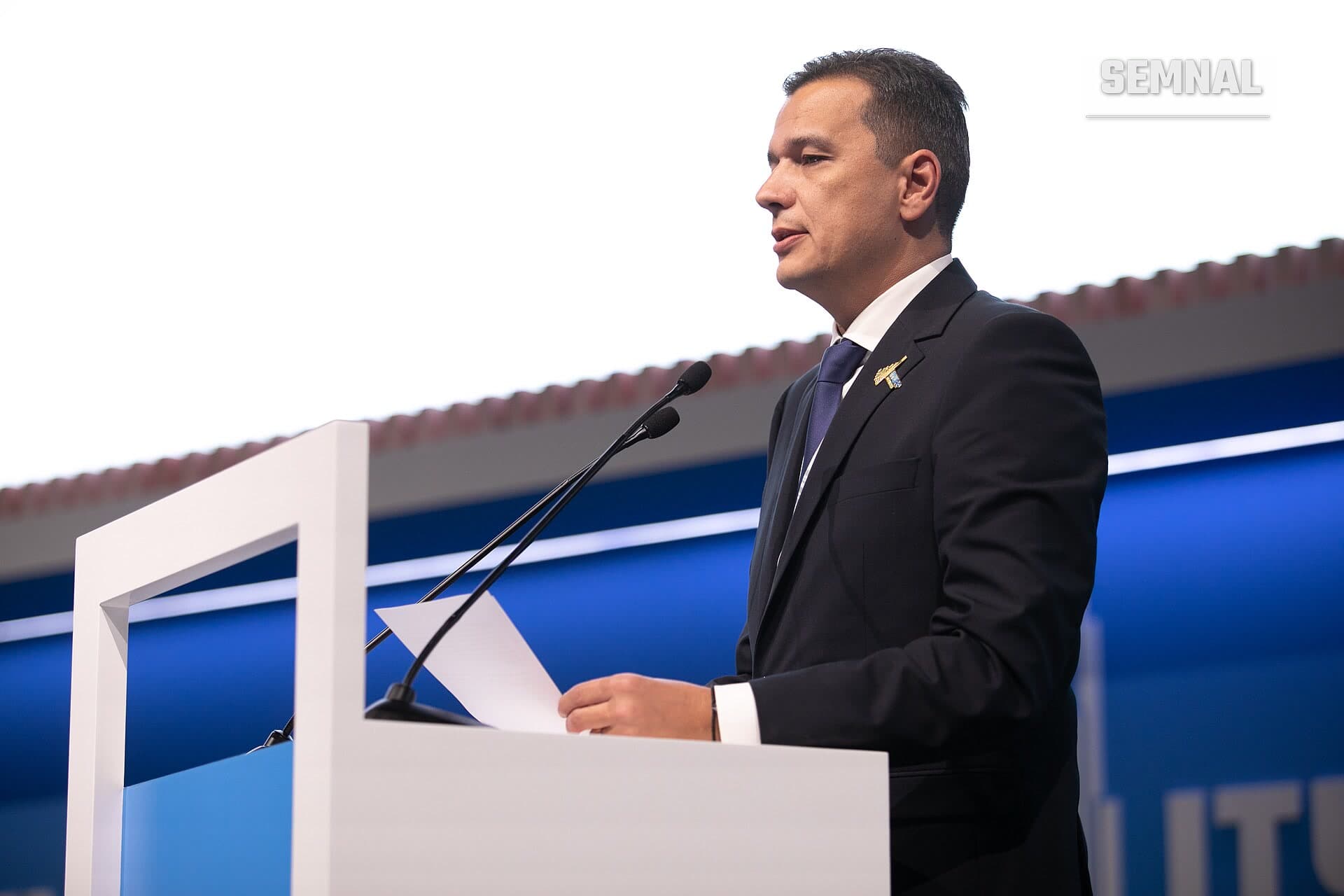 Sorin Grindeanu vorbind la o podium în costum negru și cravată albastră, la un eveniment oficial. (Foto: ITU Pictures)