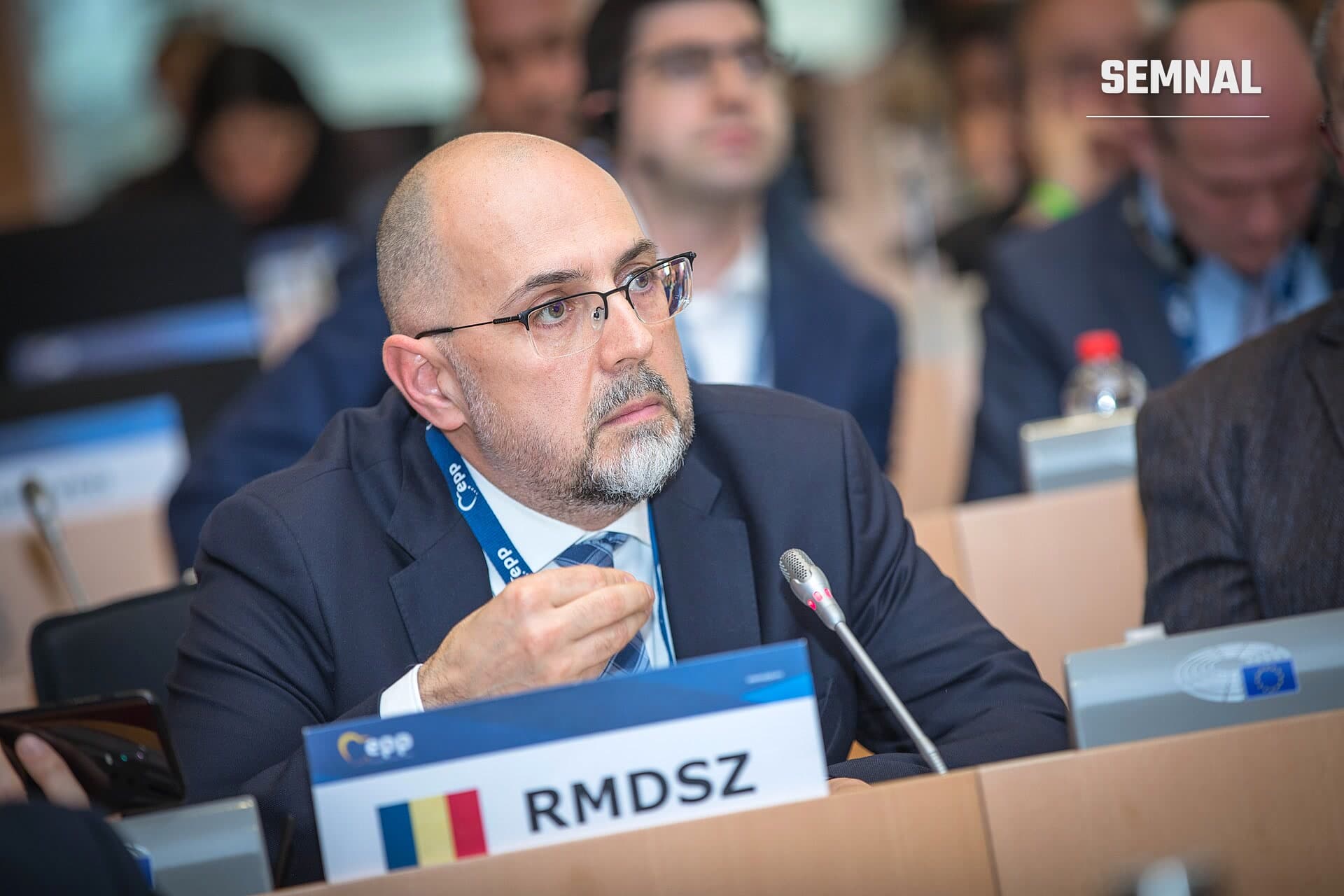 Kelemen Hunor, liderul UDMR, la o ședință oficială, purtând costum negru și cravată albastră, vorbind la o conferință cu placa de identificare RMDSZ în fața sa. (Foto: European People's Party)