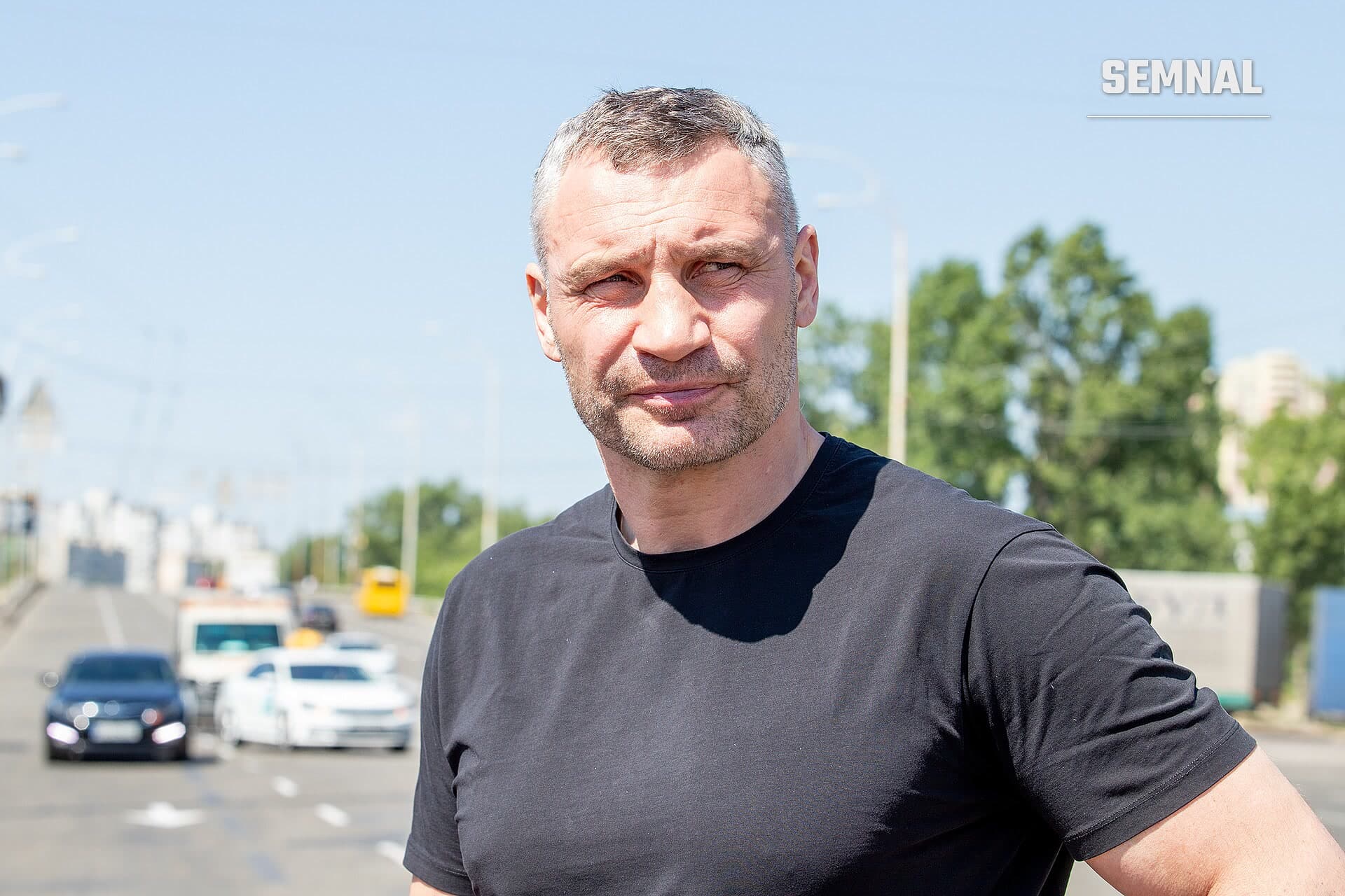Vitali Klitșko, primarul Kievului, într-o fotografie în aer liber, purtând tricou negru, cu fața vizibilă și expresie serios atentă, cu un loc de parcare și mașini în fundal estompat. (Foto: Київська міська державна адміністрація Київська міська рада)