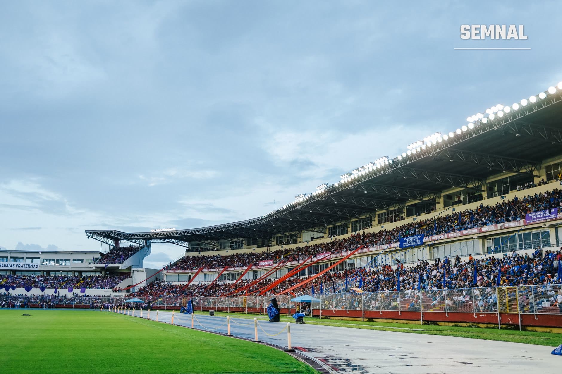 Vedere generală a unui stadion de fotbal modern cu tribune aglomerate de suporteri, teren verde bine întreținut și acoperire metalică cu iluminare puternică, în ziua unui meci important. (Foto: Luis Quintero / Pexels)