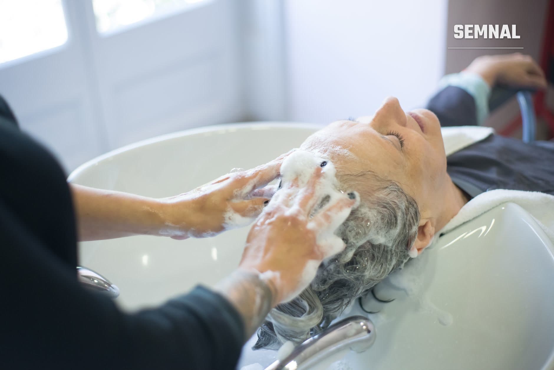 Spălarea scalpului unei persoane cu părul gri într-un bazin alb; mâini aplică șampon și masează scalpul pentru curățare și îngrijire. (Foto: Kampus Production / Pexels)