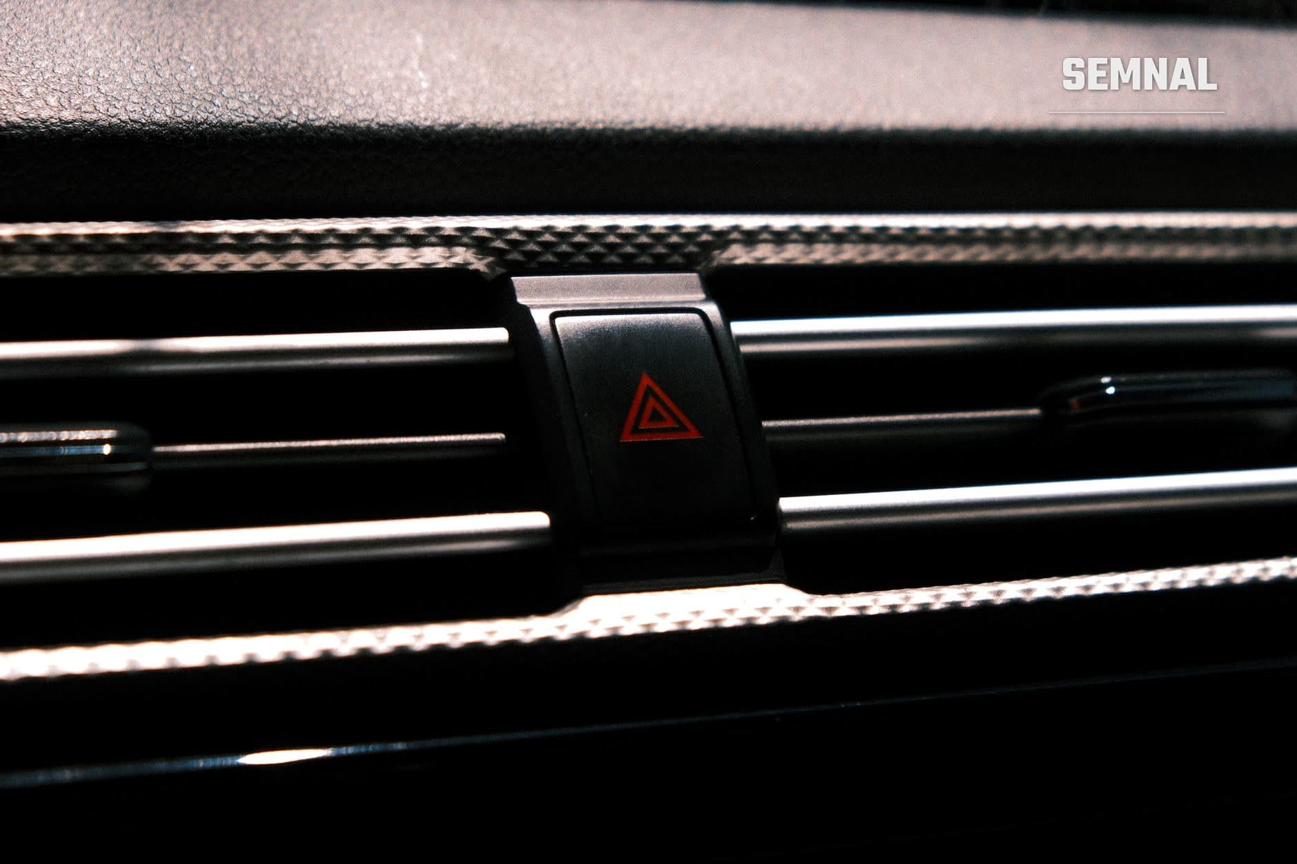 Buton de avarie cu simbol triunghi roșu pe tabloul de bord negru al unei mașini, ilustrând indicatoarele și avertismentele din interiorul autoturismului. (Foto: John Joshua Mejia Jose / Pexels)
