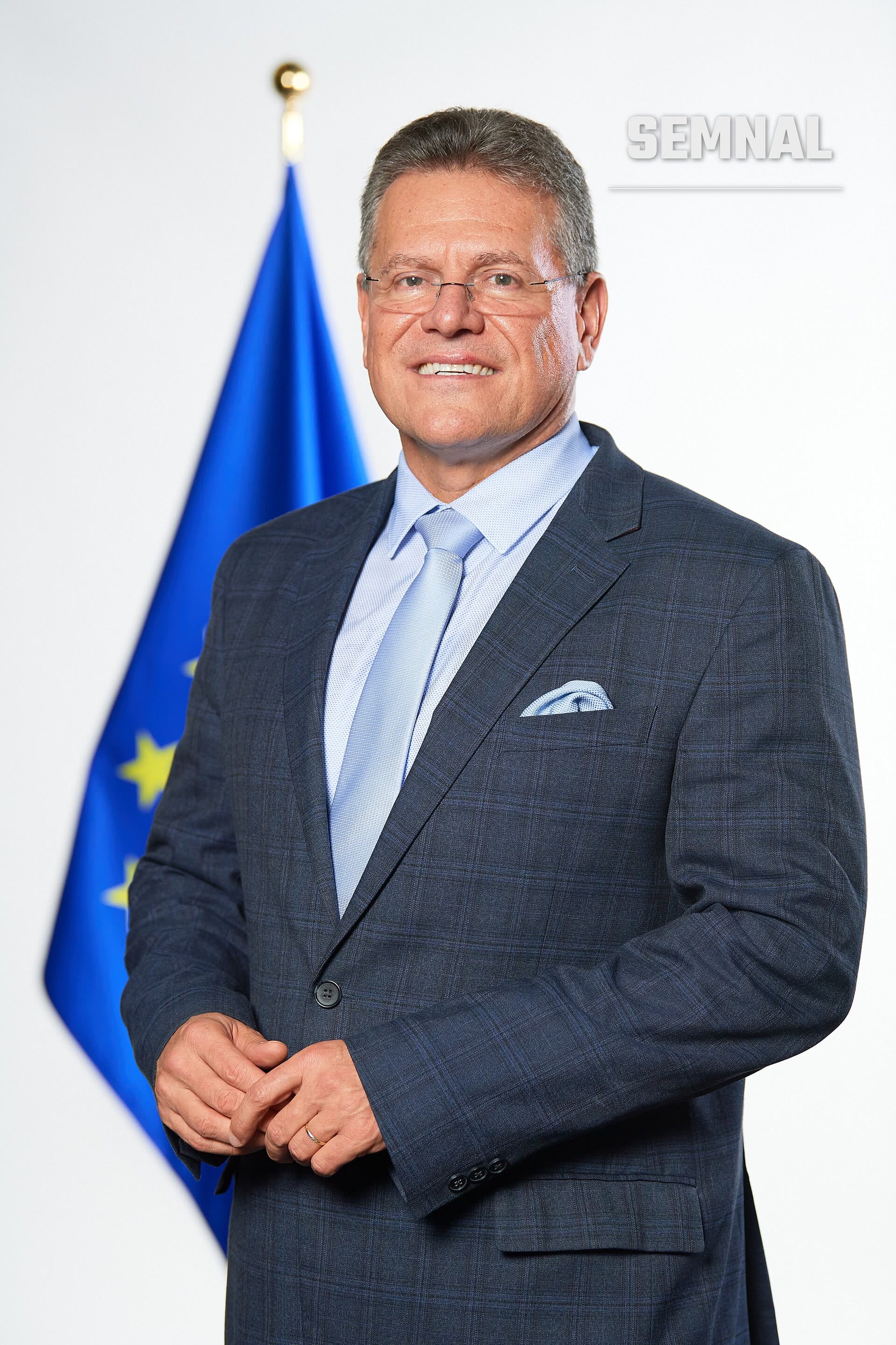 Maroš Šefčovič, comisar european pentru comerț, într-un portret oficial purtând costum gri și cravată bleu, cu steagul Uniunii Europene în fundal. (Foto: European Commission Audiovisual Service)