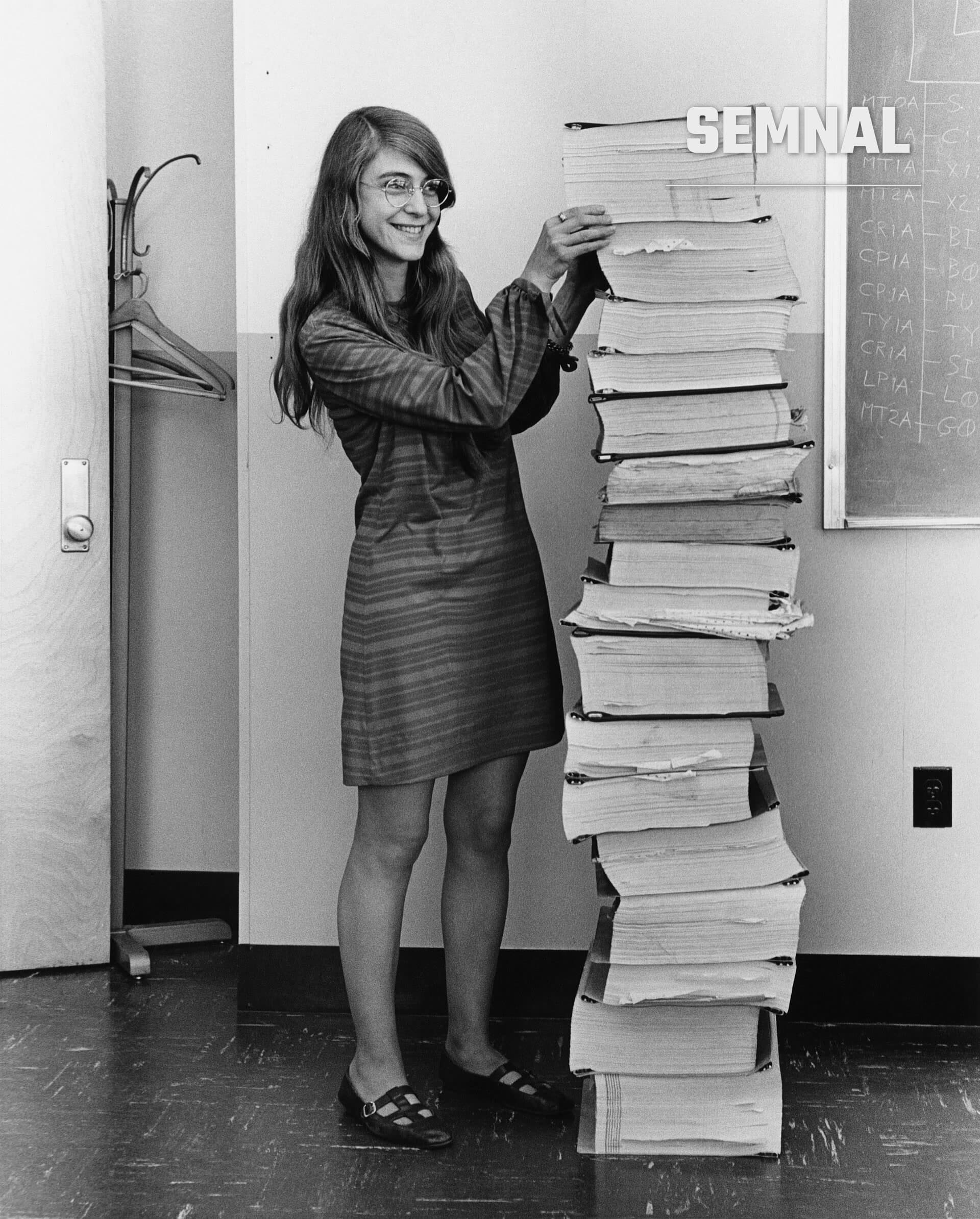 Margaret Hamilton, informaticiana și inginer software, zâmbind lângă o stivă impresionantă de cărți și dosare în birou (Foto: Adam Cuerden)