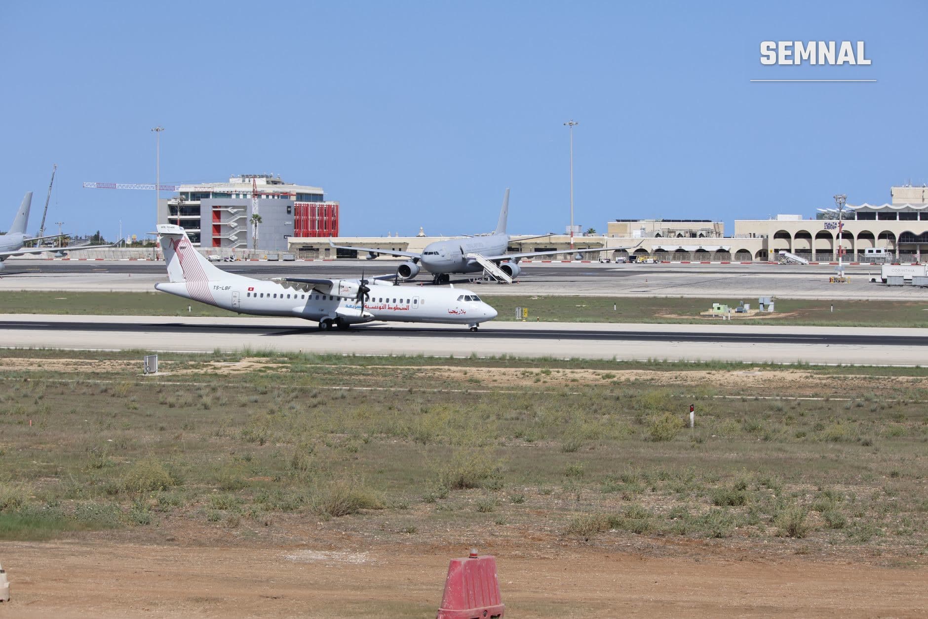 Avion ATR 72 parcat pe pista unui aeroport cu alte aeronave și terminale in fundal sub cer albastru (Foto: Drinu Cutajar / Pexels)
