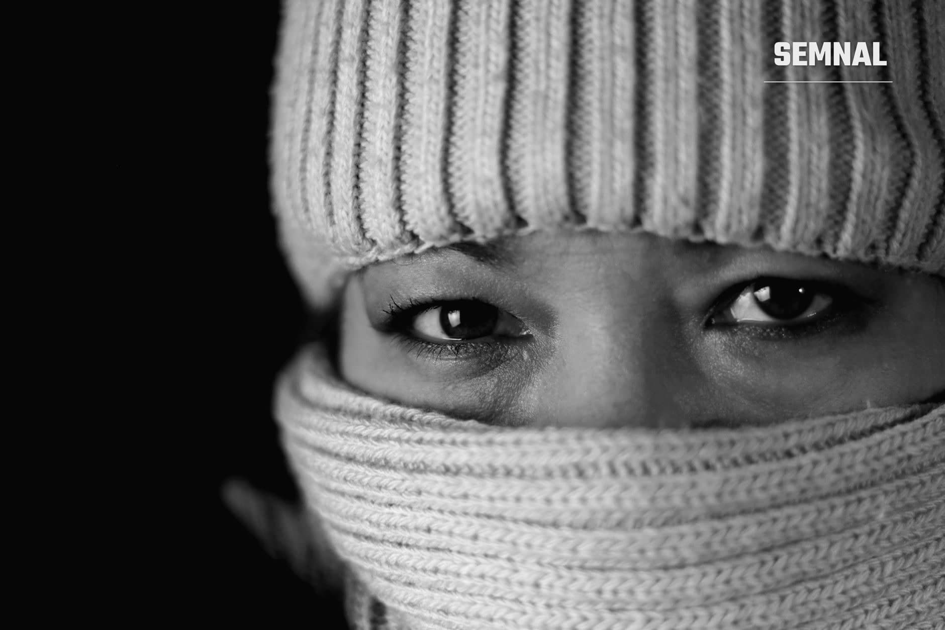 Portret alb-negru al unei persoane învelite în eșarfă tricotată gri, cu ochii intensi privindu direct în cameră, ilustrând protecția împotriva frigului și senzația termică. (Foto: Marek Kupiec / Pexels)