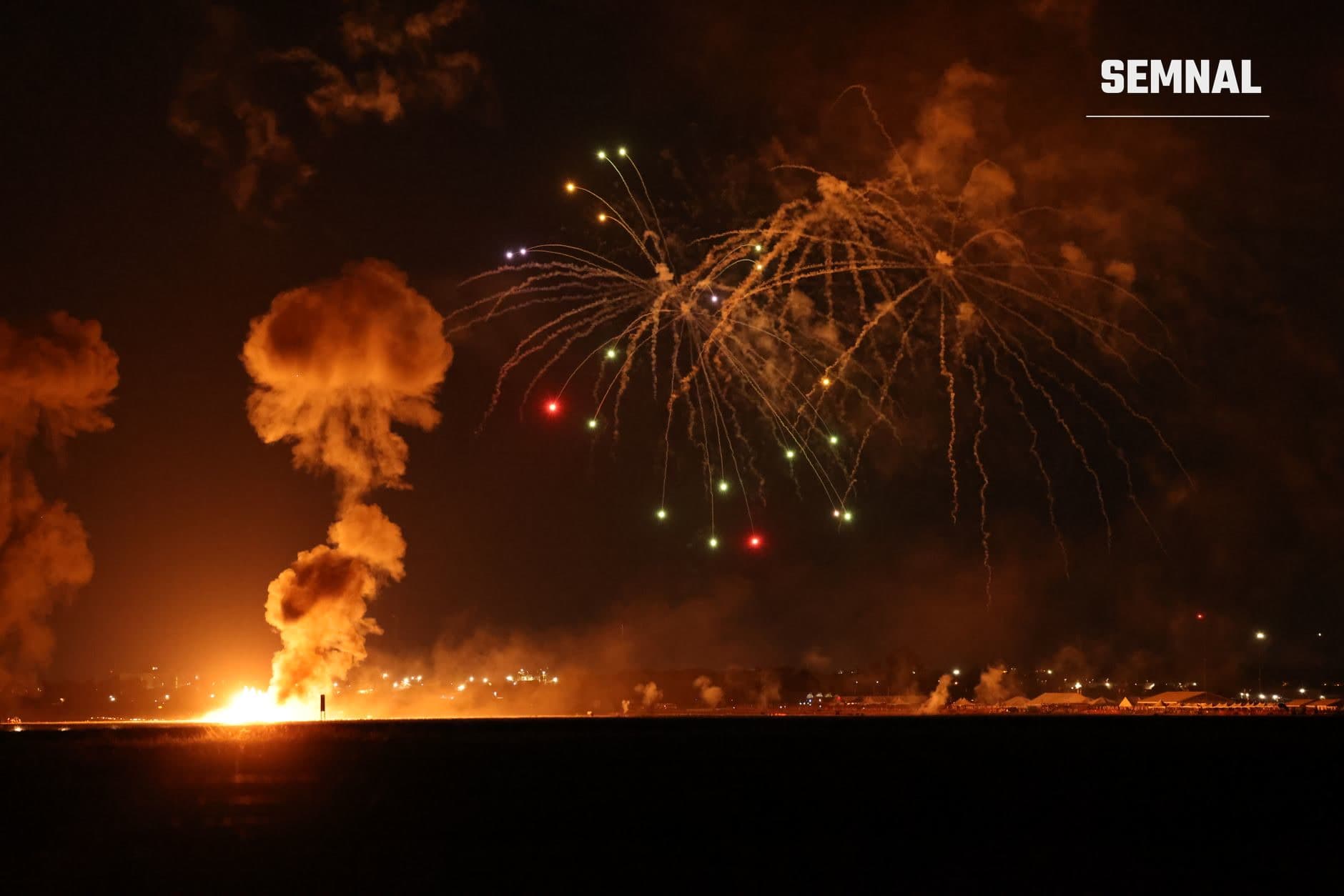 Explozie nocturnă cu flăcări și fum dens pe orizont, cu proiectile luminoase în cer negru, ilustrând un atac aerian sau bombardament militar. (Foto: Sean P. Twomey / Pexels)