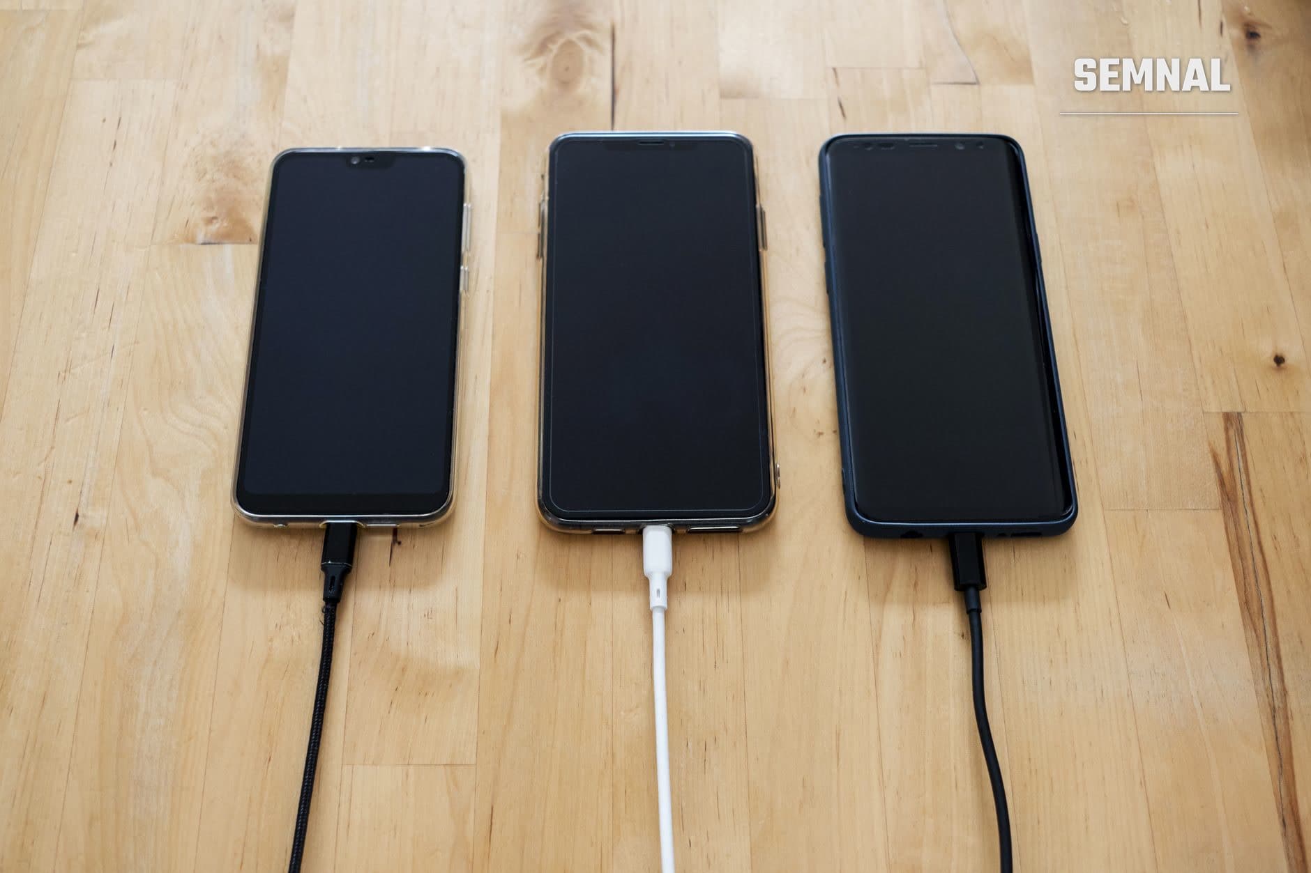 Trei telefoane mobile cu ecranele stinse, așezate pe o masă de lemn și conectate la cabluri de încărcare. (Foto: Stanley Ng / Pexels)