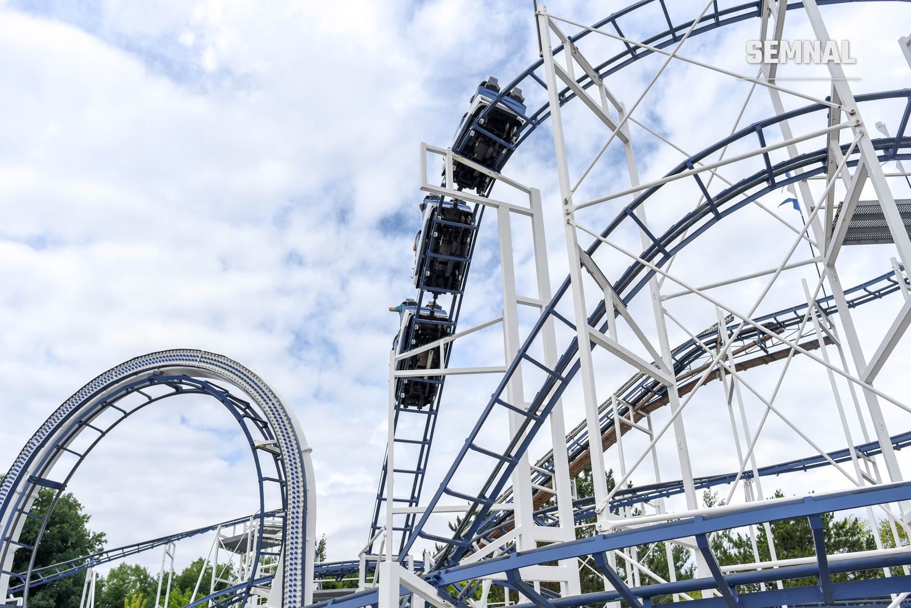 Roller coaster cu structură metalică și albastră, cărucioară pe pantă verticală și buclă în stânga, sub cer noros (Foto: Element5 Digital / Pexels)