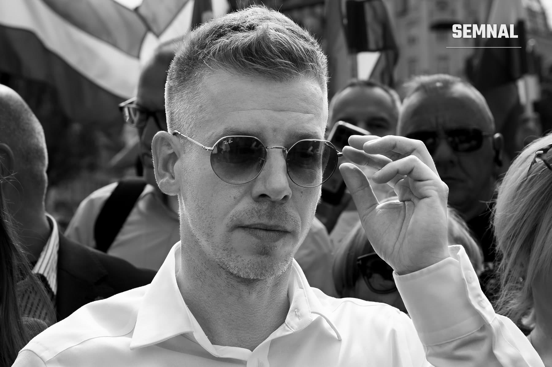 Péter Magyar: bărbat cu păr scurt, ochelari de soare rotunzi și cămașă albă, cu mâna ridicată spre ochelari, într-o mulțime; fotografie alb-negru. (Foto: B. Molnár Béla)
