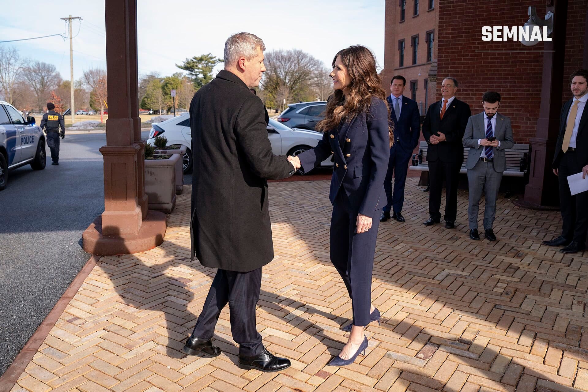 Cătălin Predoiu, ministrul interimar al Afacerilor Interne, salută o persoană în costum bleumarin la un eveniment oficial în fața unei clădiri publice. (Foto: DHSgov)