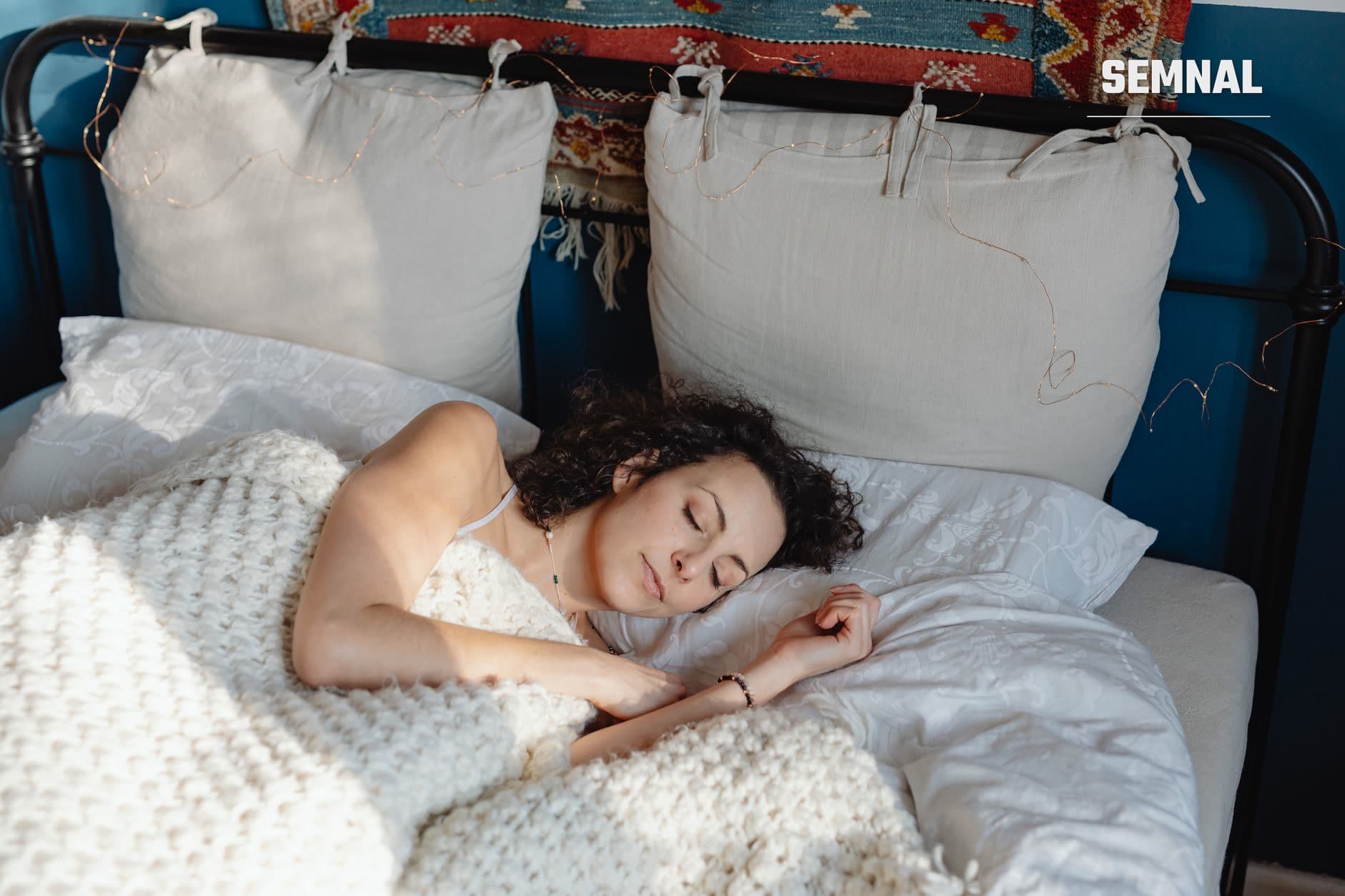 Femeie cu părul negru dormind pașnic pe un pat cu lenjerie albă, ilustrând conceptul de somn și reglare a ritmului circadian. (Foto: https://kaboompics.com/ / Pexels)