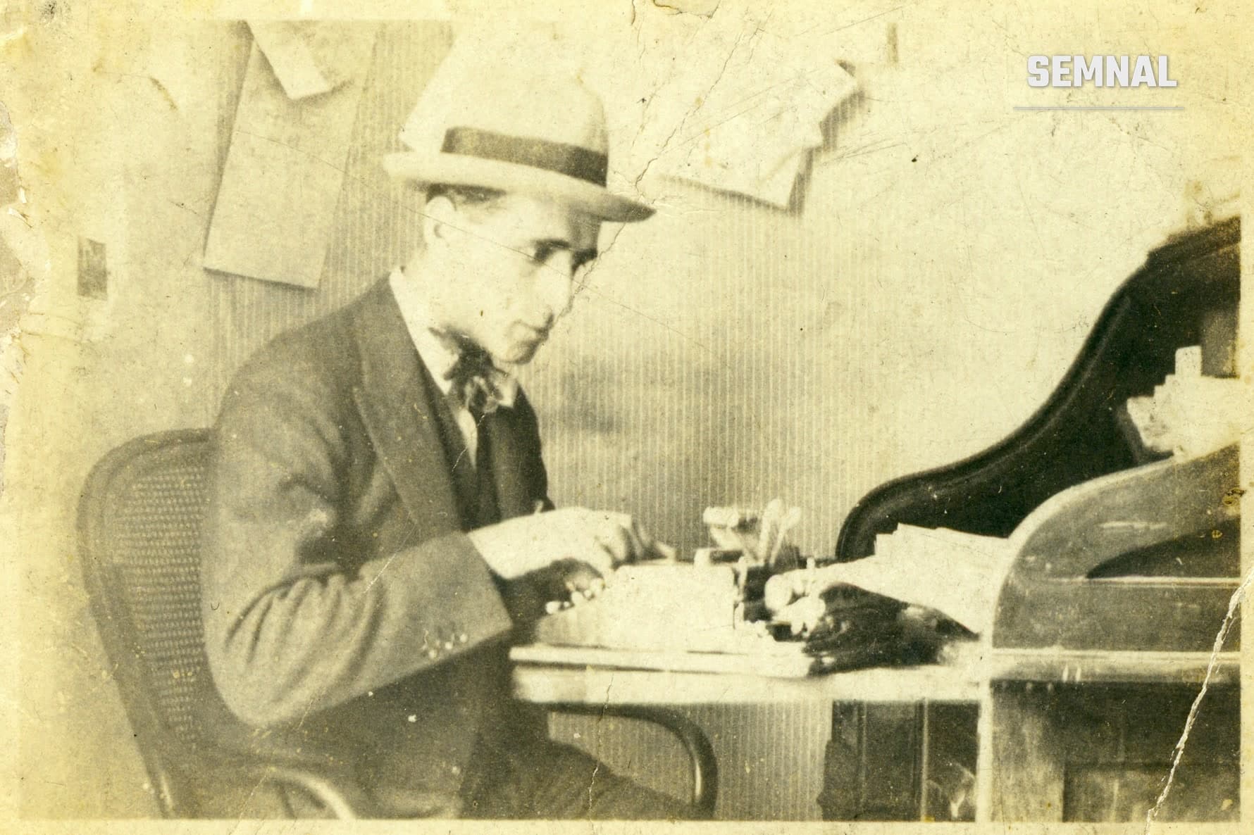 Luis Enrique, bărbat cu pălărie și costum, așezat la o mașină de scris, într-o fotografie veche în tonuri sepia (Foto: Unknown author Unknown author)