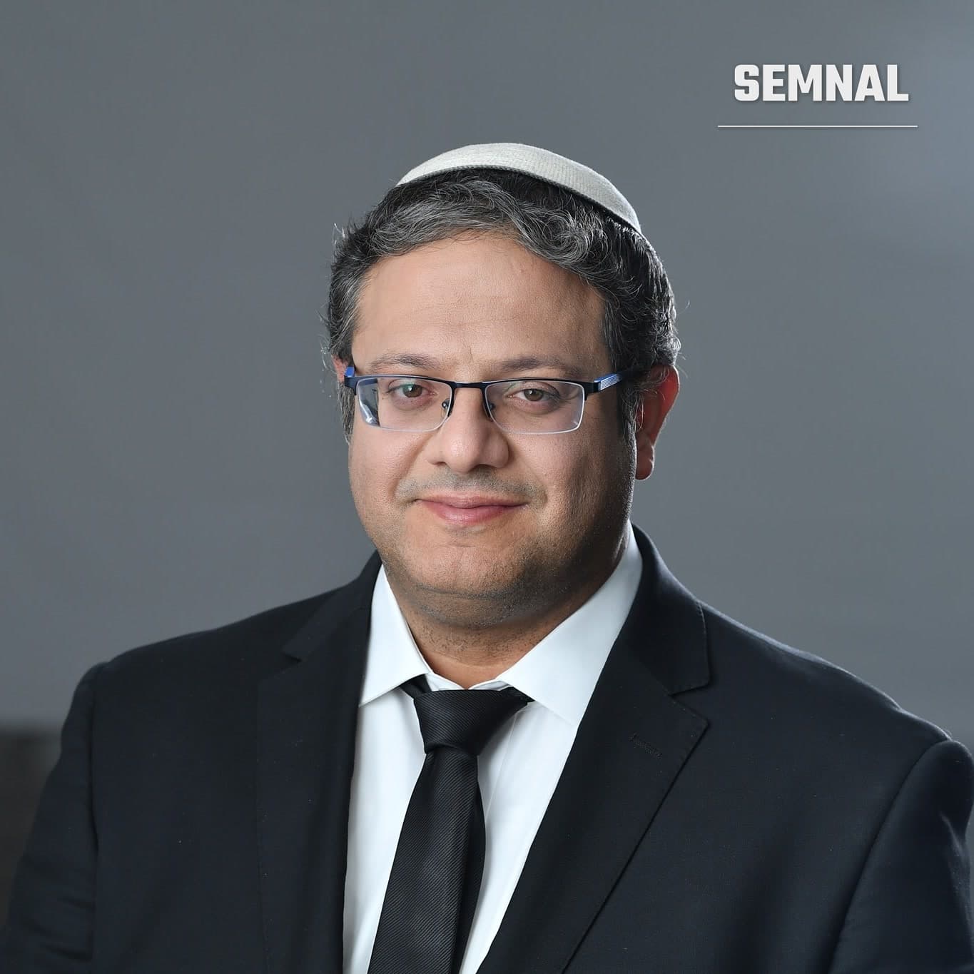 Itamar Ben-Gvir, ministrul israelian al Securității Naționale, într-un portret de studio pe fundal gri, purtând costum negru și kipa albă. (Foto: דוד דנברג)
