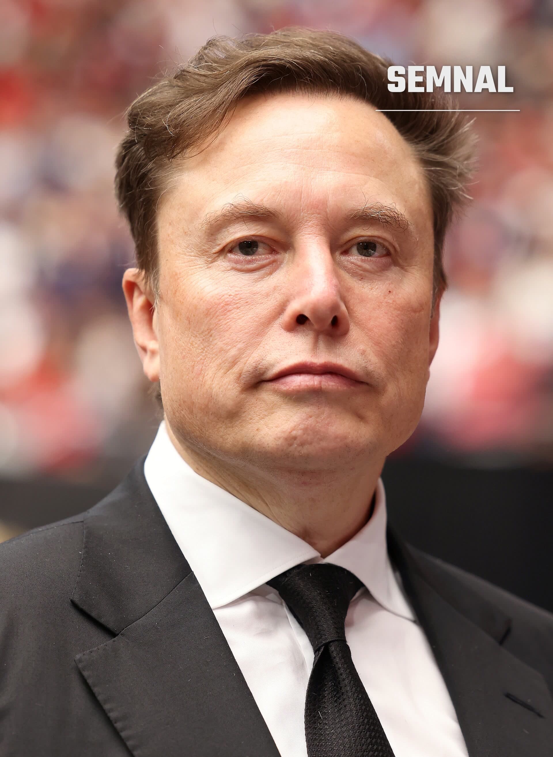 Elon Musk, directorul executiv al SpaceX, într-un costum negru, cu cămașă albă și cravată neagră, privind spre cameră pe un fundal estompat. (Foto: Gage Skidmore)