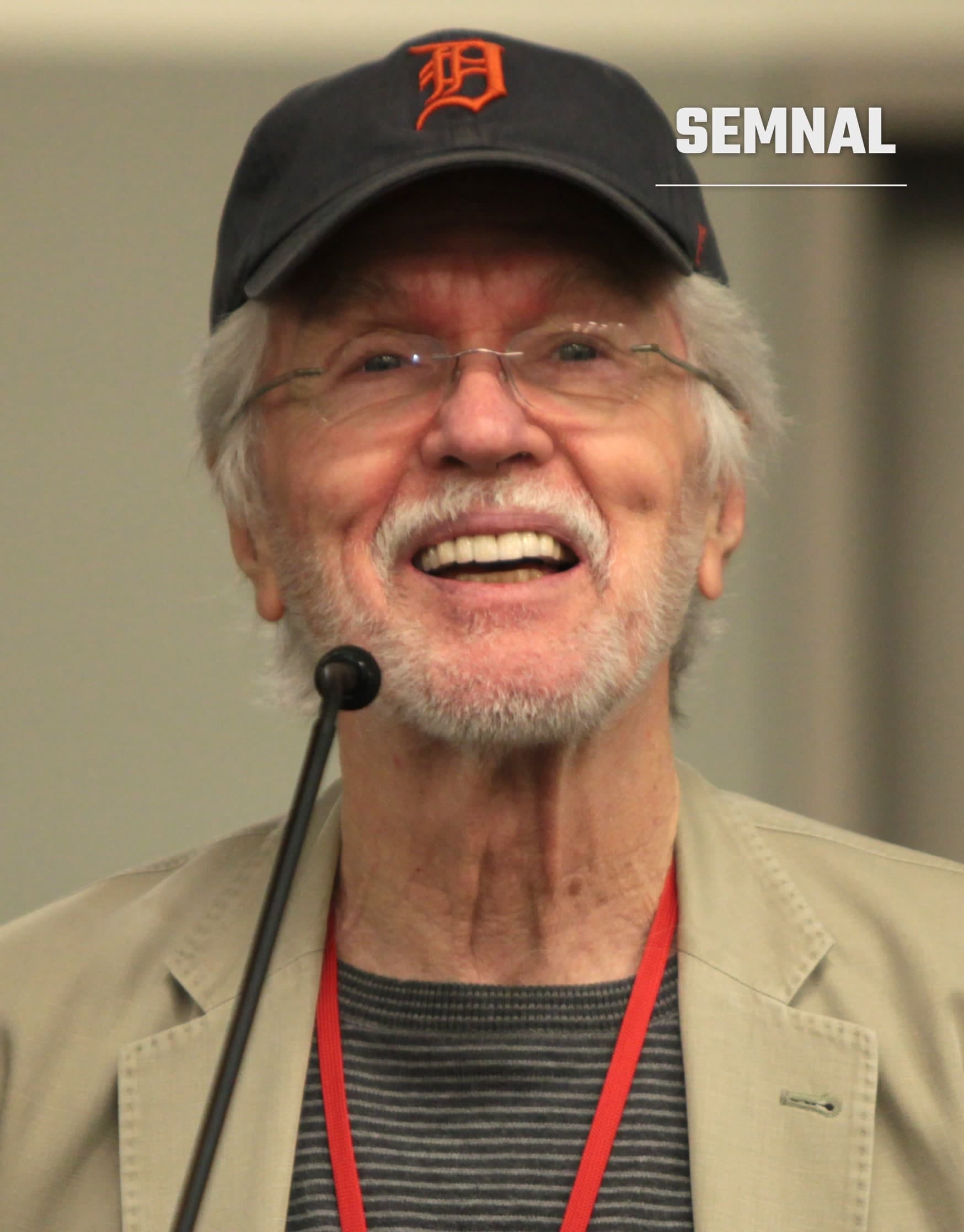 Tom Skerritt, actor american, zâmbind în fața unui microfon, purtând o șapcă neagră și ochelari cu rama subțire (Foto: Gage Skidmore)