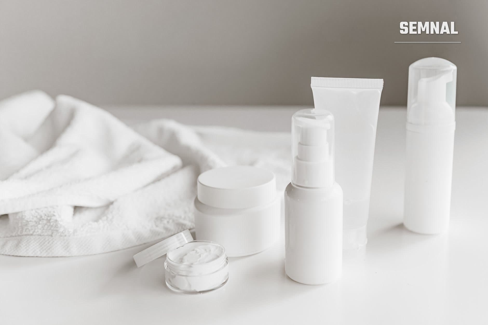 Recipiente cosmetice albe, fără etichetă, cu cremă deschisă într-un borcan, pe o masă albă lângă un prosop alb (Foto: ROMAN ODINTSOV / Pexels)