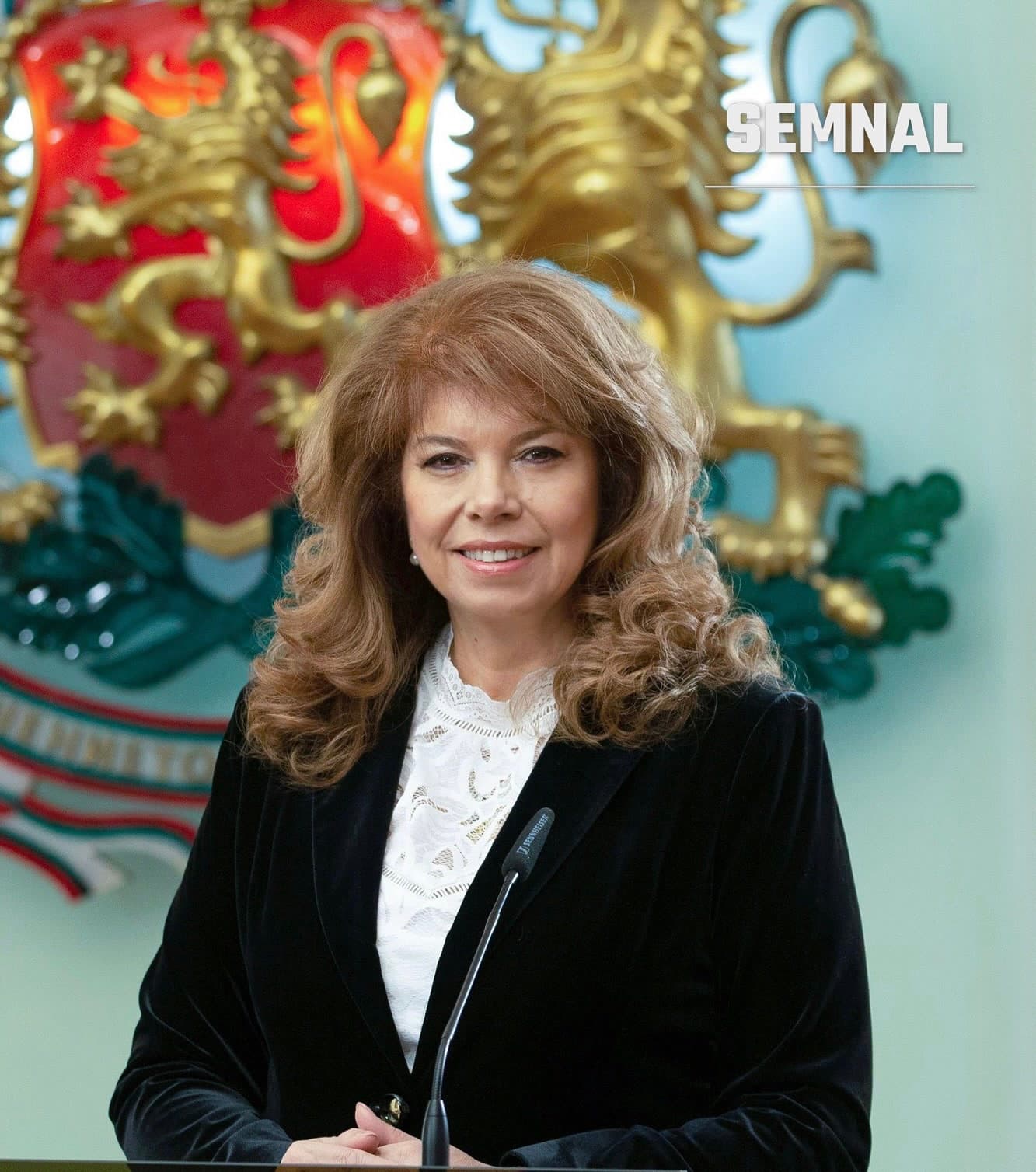 Iliana Iotova, zâmbind în fața unui microfon, cu stema Bulgariei în fundal, într-o fotografie de presă. (Foto: Unknown author Unknown author)