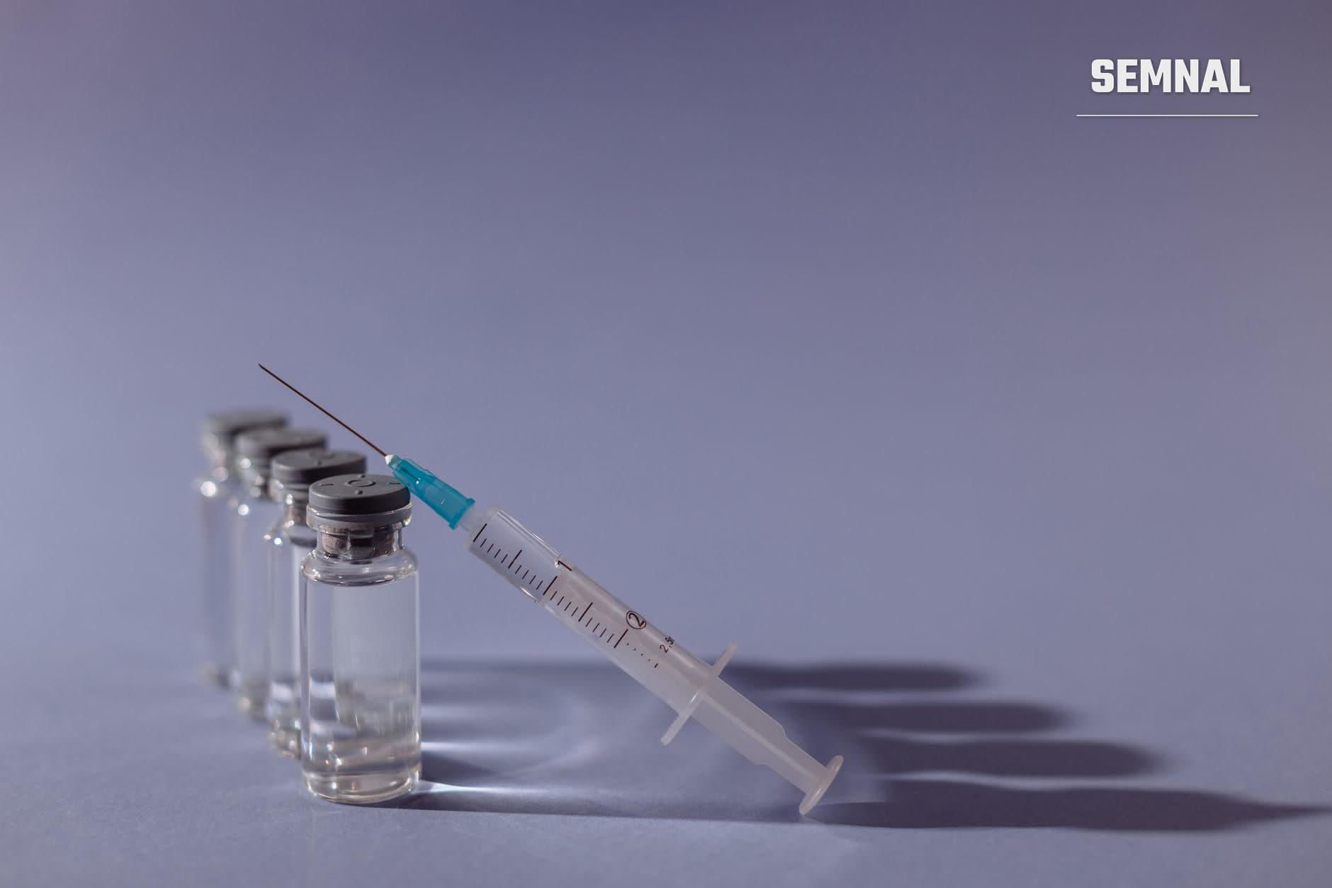 Flacoane de sticlă cu dopuri gri și o seringă cu ac albastru, pe un fundal gri-violet, care sugerează vaccinarea. (Foto: Thirdman / Pexels)